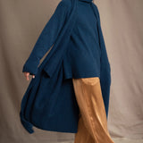 Woman wearing a long cashmere coat in teal blue over teal blue cashmere turtleneck sweater and bronze silk trousers