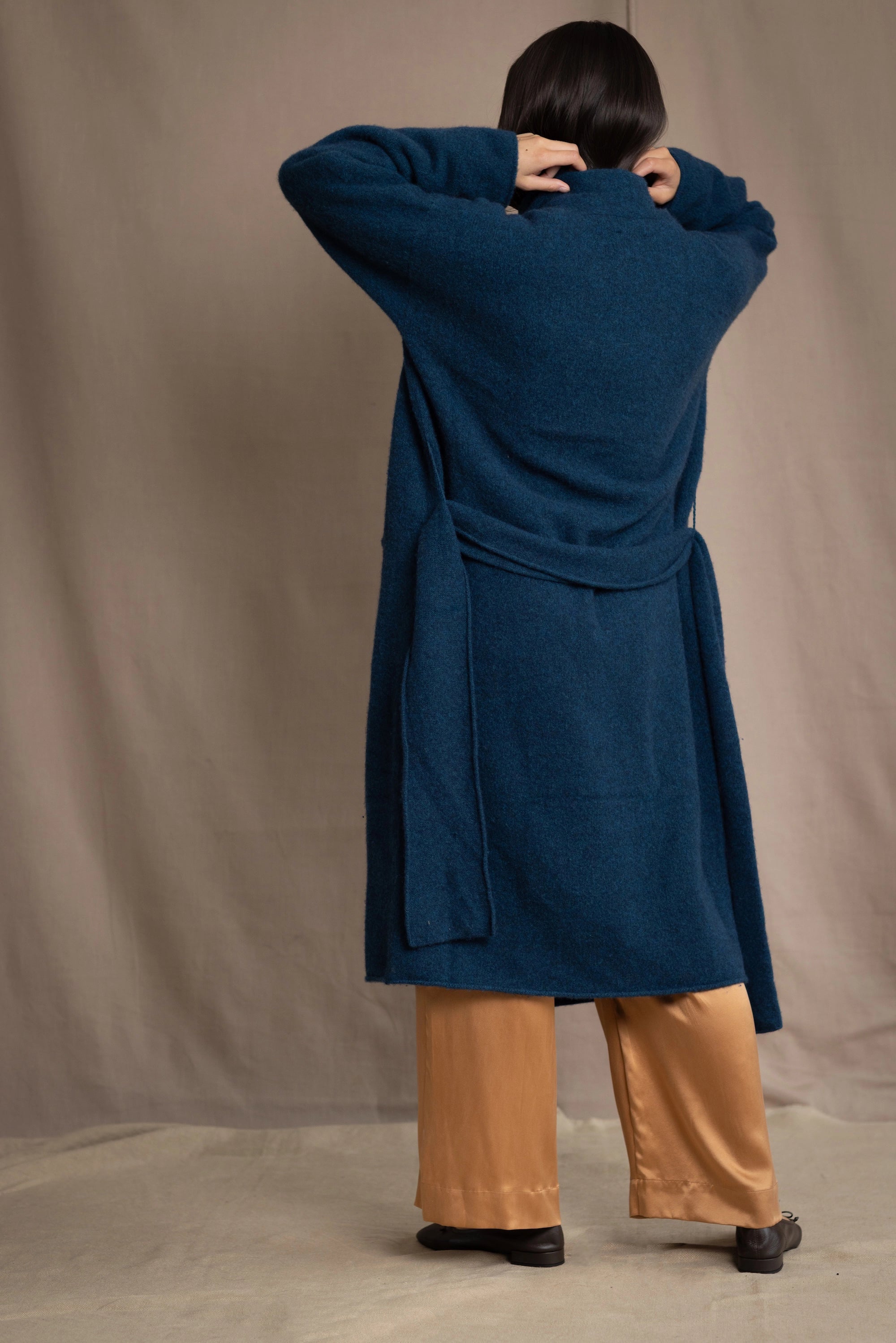 Woman wearing a long cashmere coat in teal blue over teal blue cashmere turtleneck sweater and bronze silk trousers