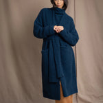 Woman wearing a long cashmere coat in teal blue over teal blue cashmere turtleneck sweater and bronze silk trousers