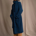 Woman wearing a long cashmere coat in teal blue over teal blue cashmere turtleneck sweater and bronze silk trousers