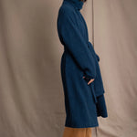 Woman wearing a long cashmere coat in teal blue over teal blue cashmere turtleneck sweater and bronze silk trousers