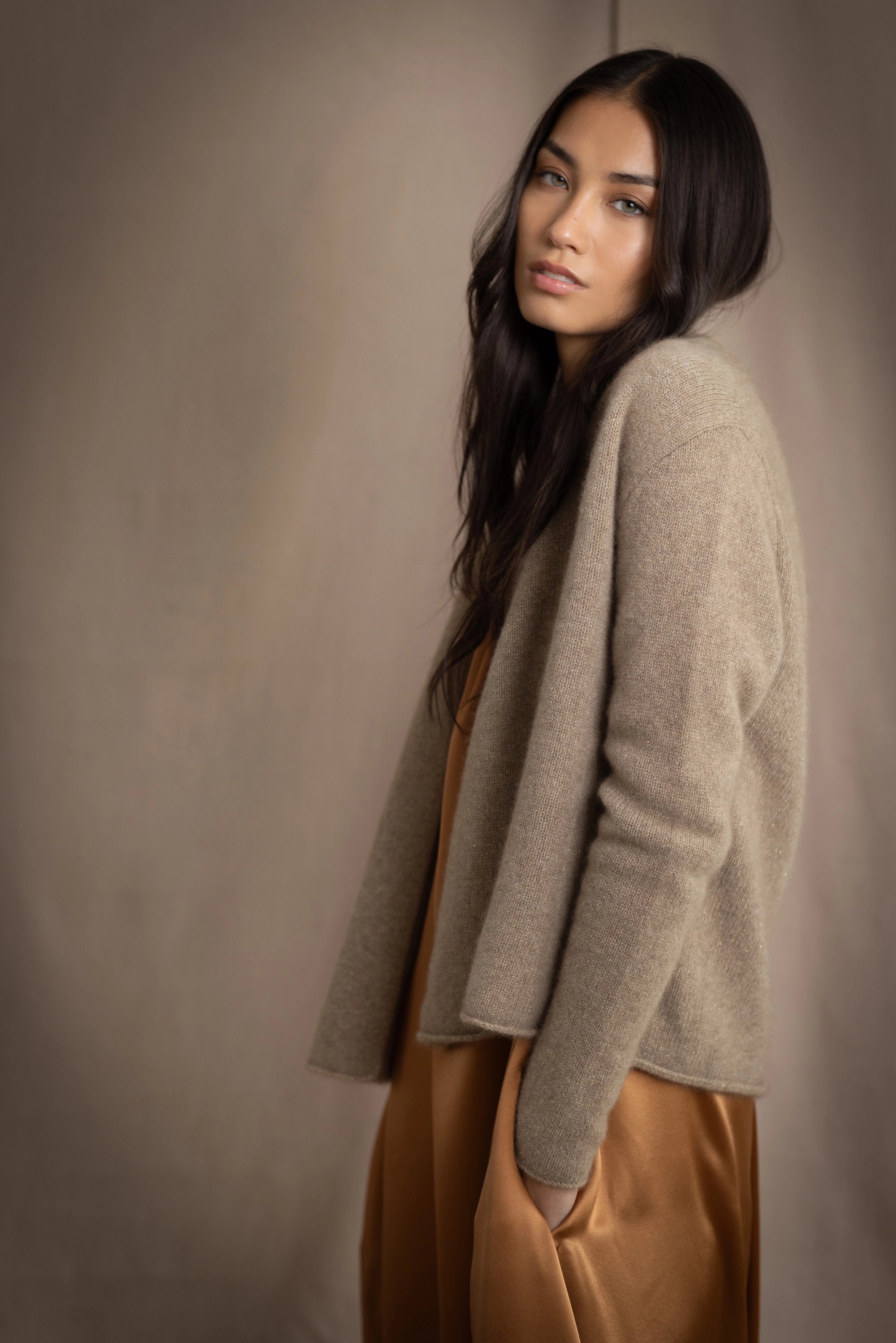 woman wearing a beige cashmere cardigan with gold metallic lurex thread over a bronze silk dress