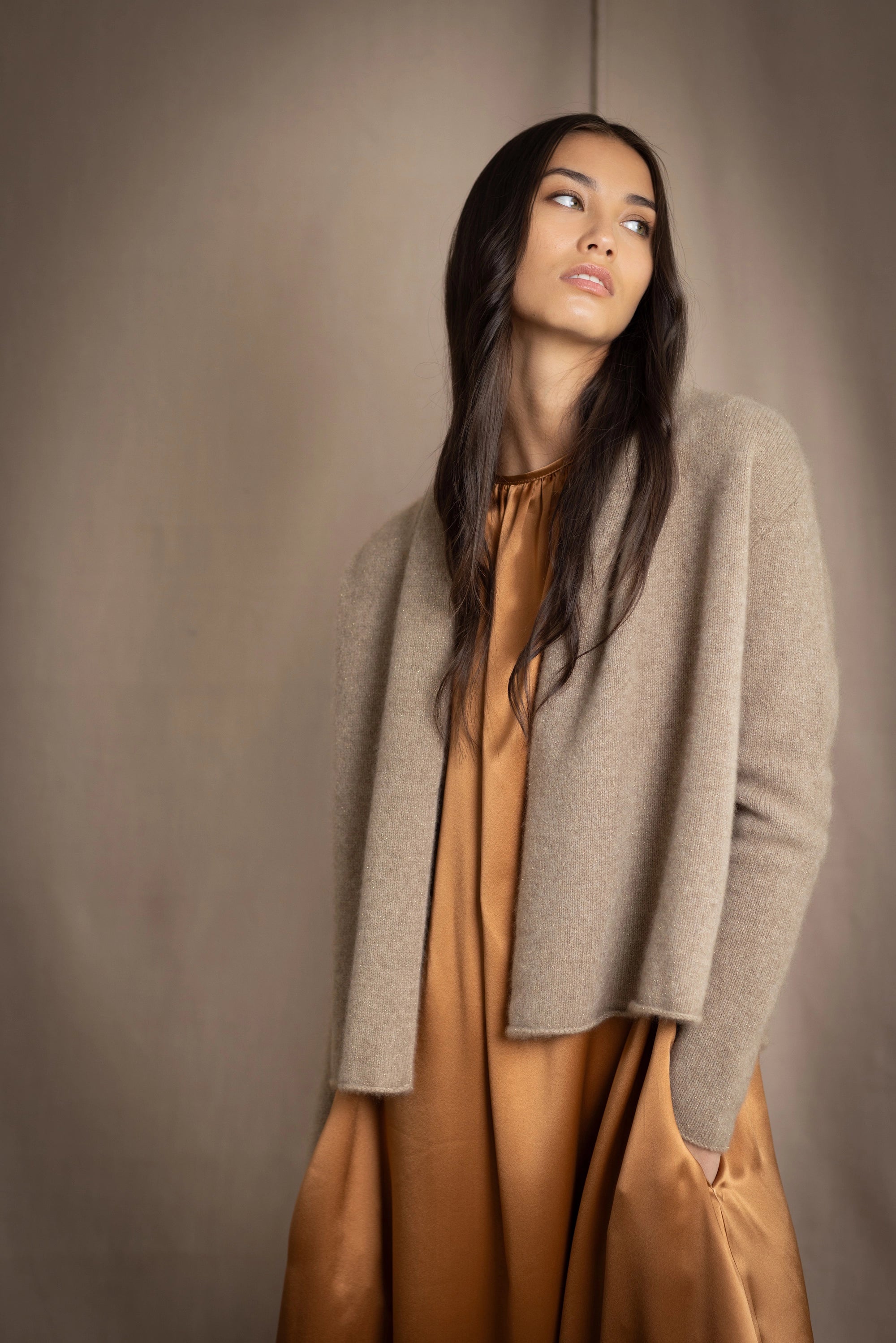 woman wearing a beige cashmere cardigan with gold metallic lurex thread over a bronze silk dress