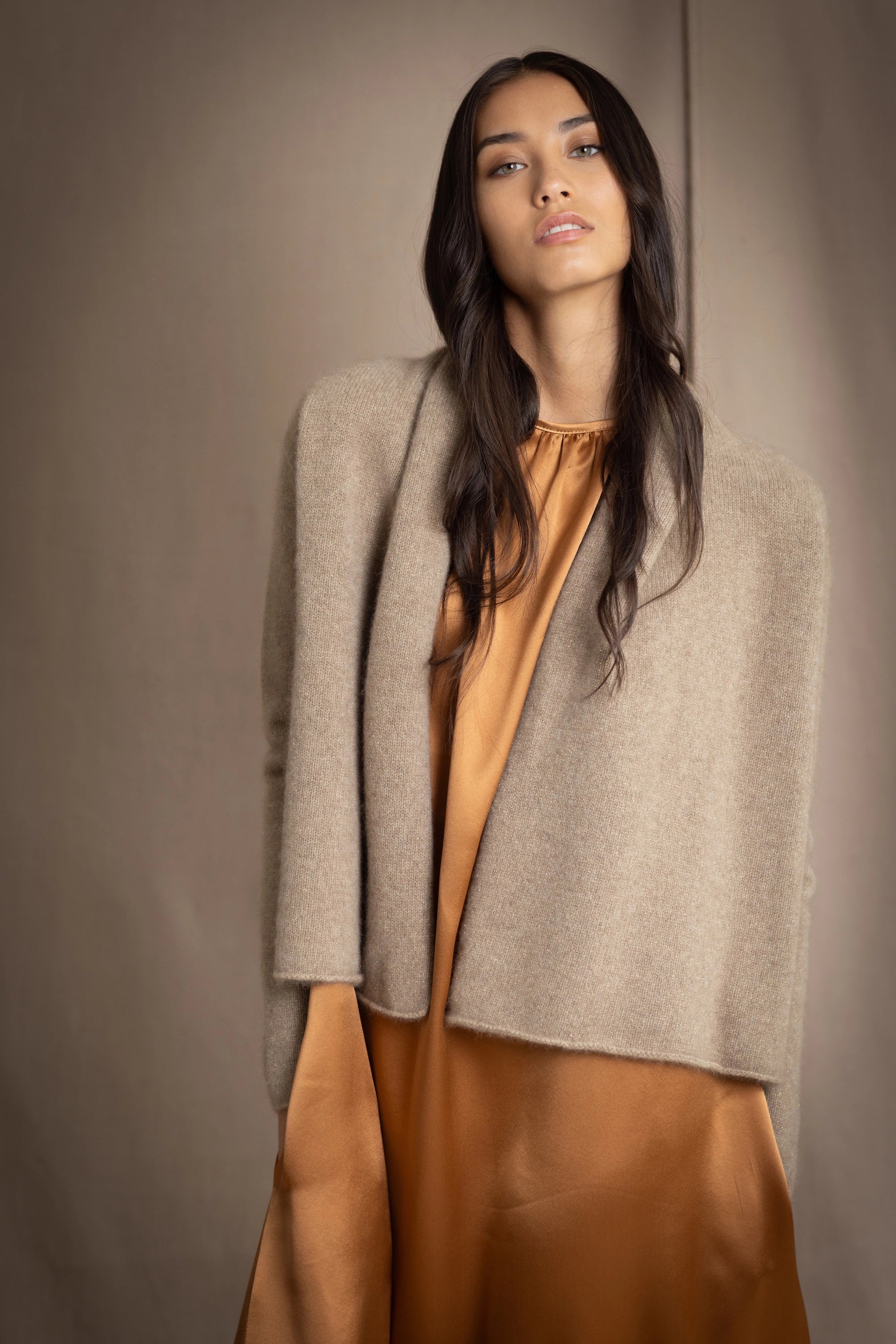 woman wearing a beige cashmere cardigan with gold metallic lurex thread over a bronze silk dress