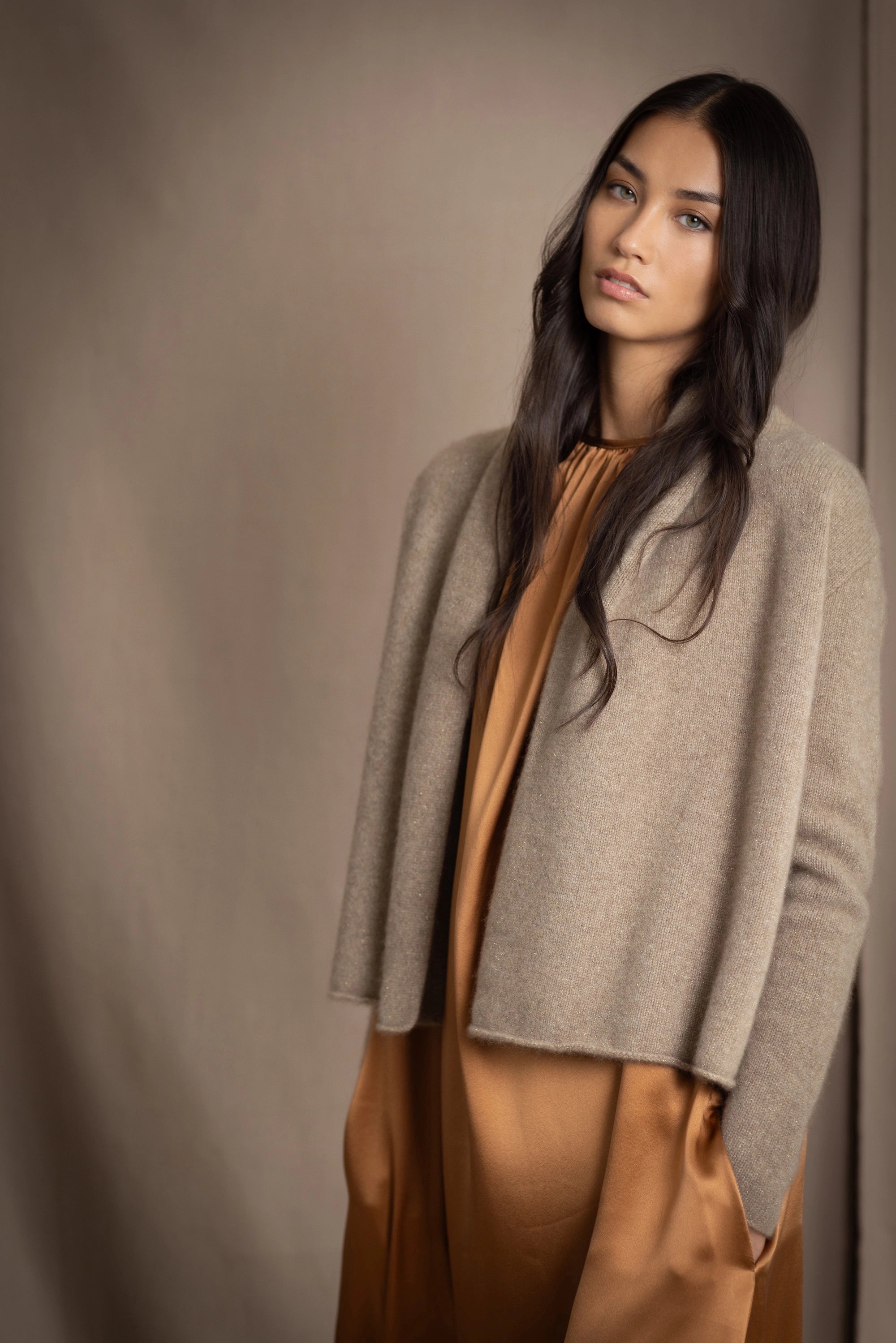 woman wearing a beige cashmere cardigan with gold metallic lurex thread over a bronze silk dress