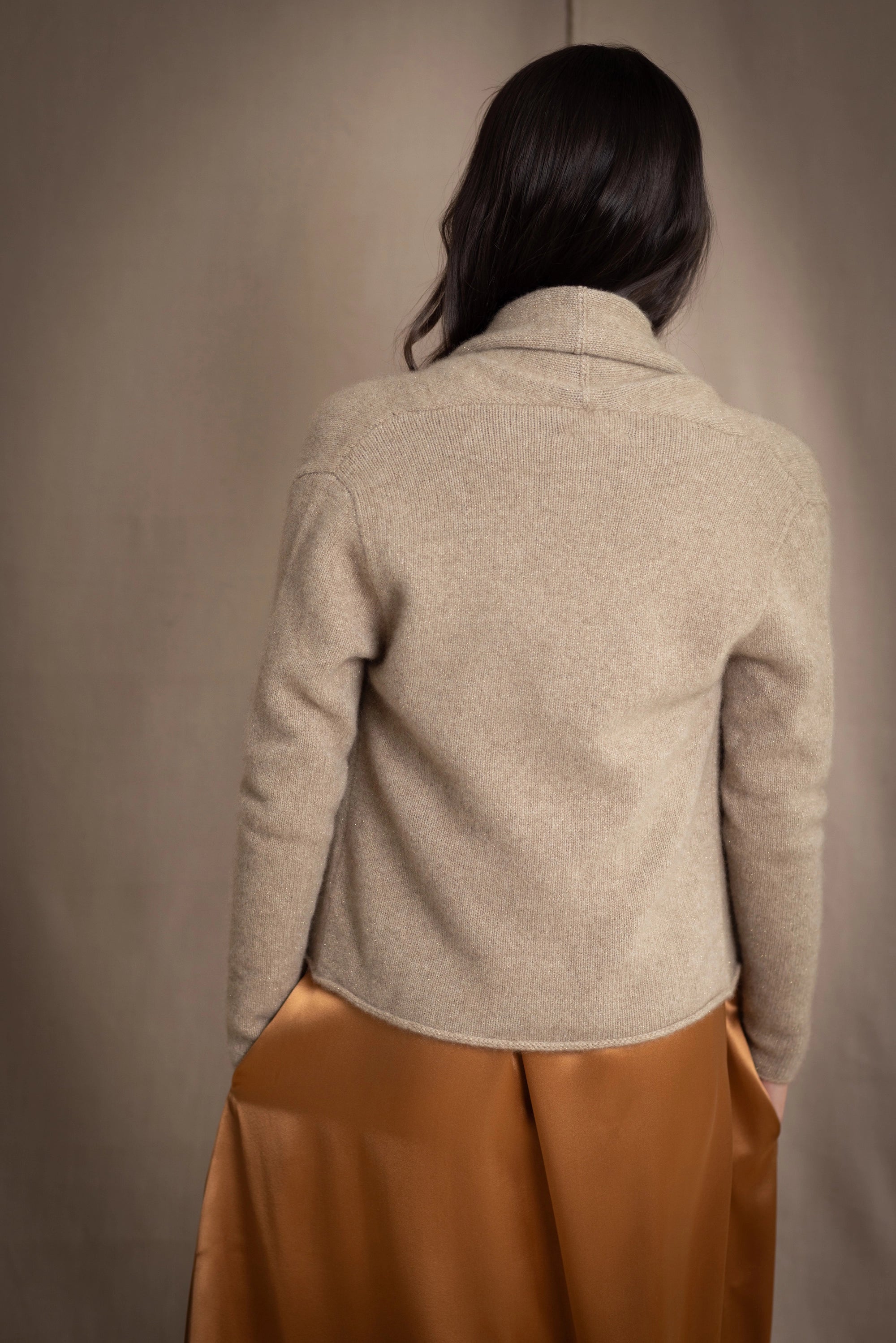 woman wearing a beige cashmere cardigan with gold metallic lurex thread over a bronze silk dress