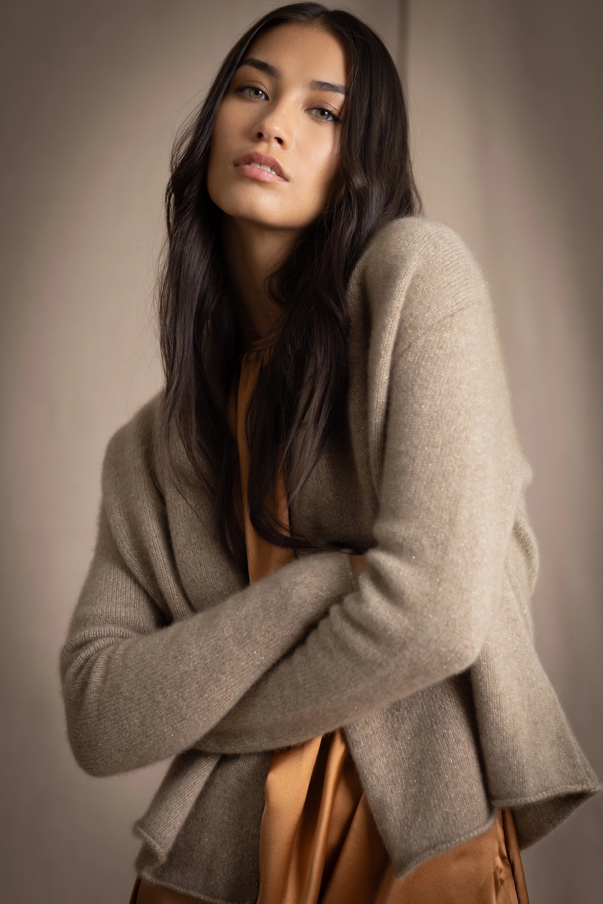 woman wearing a beige cashmere cardigan with gold metallic lurex thread over a bronze silk dress