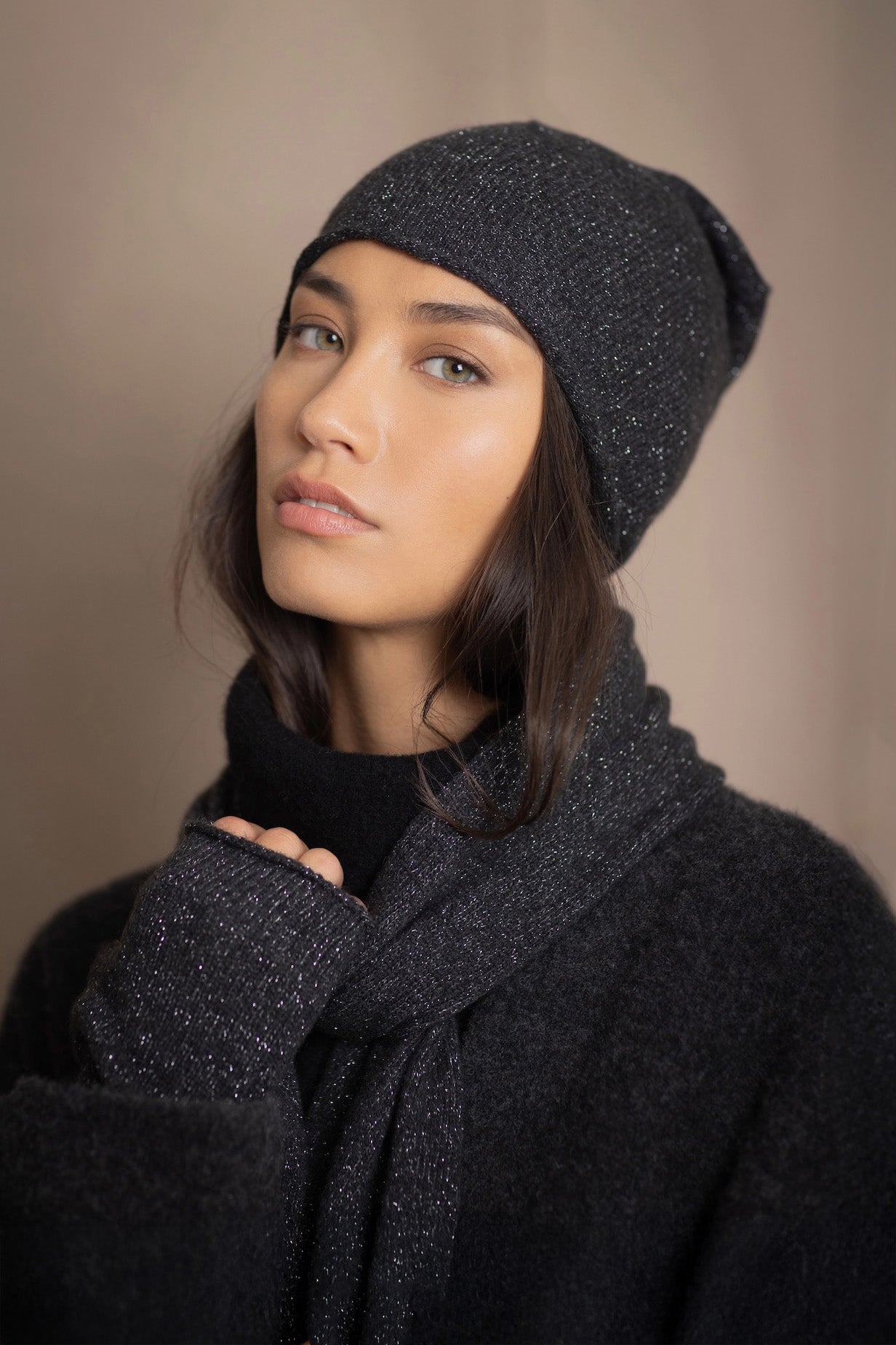Woman wearing a cashmere beanie hat, cashmere scarf and cashmere gloves with cashmere sweater in black with silver metallic thread