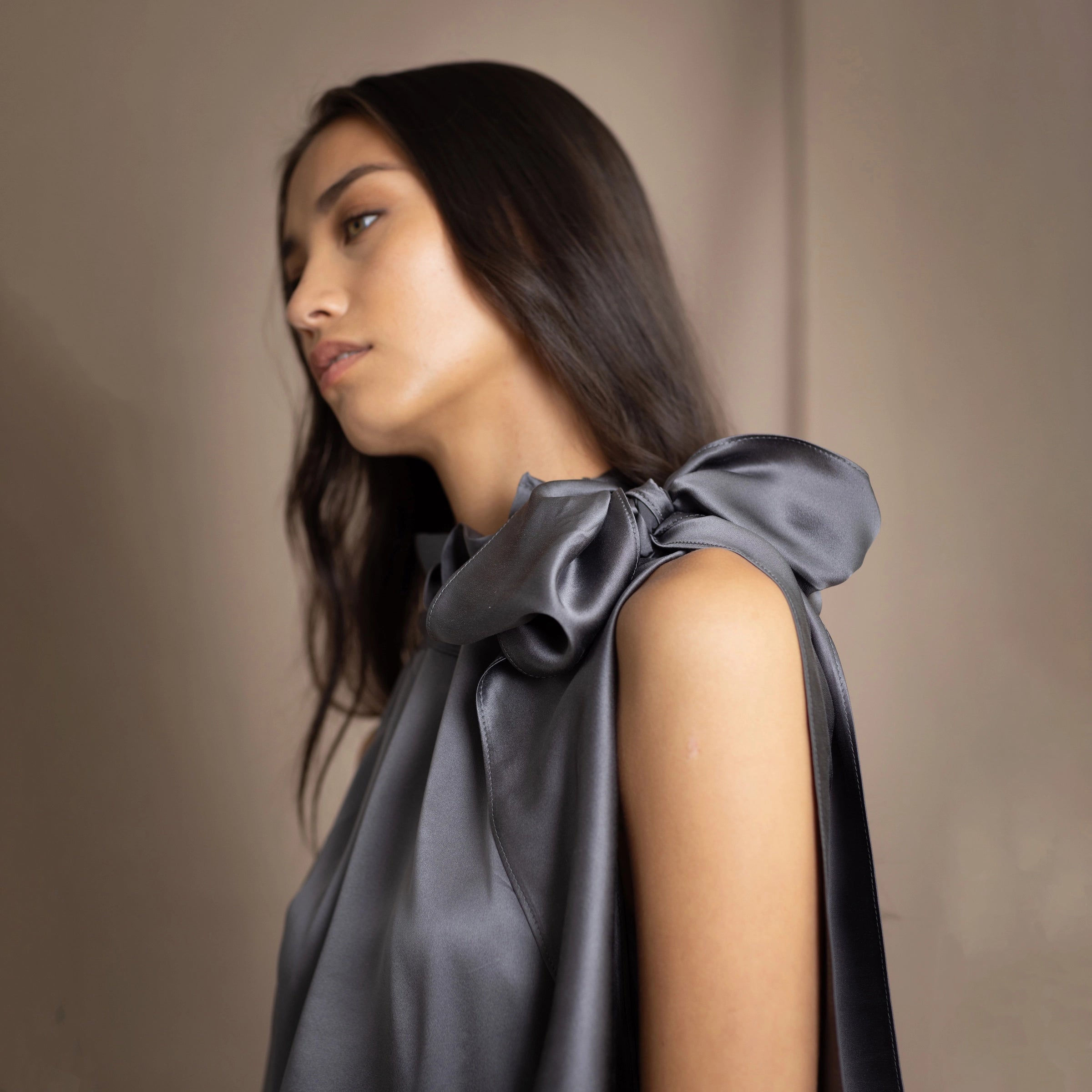 Woman wearing a silk top with a bow around the neckline in pewter grey