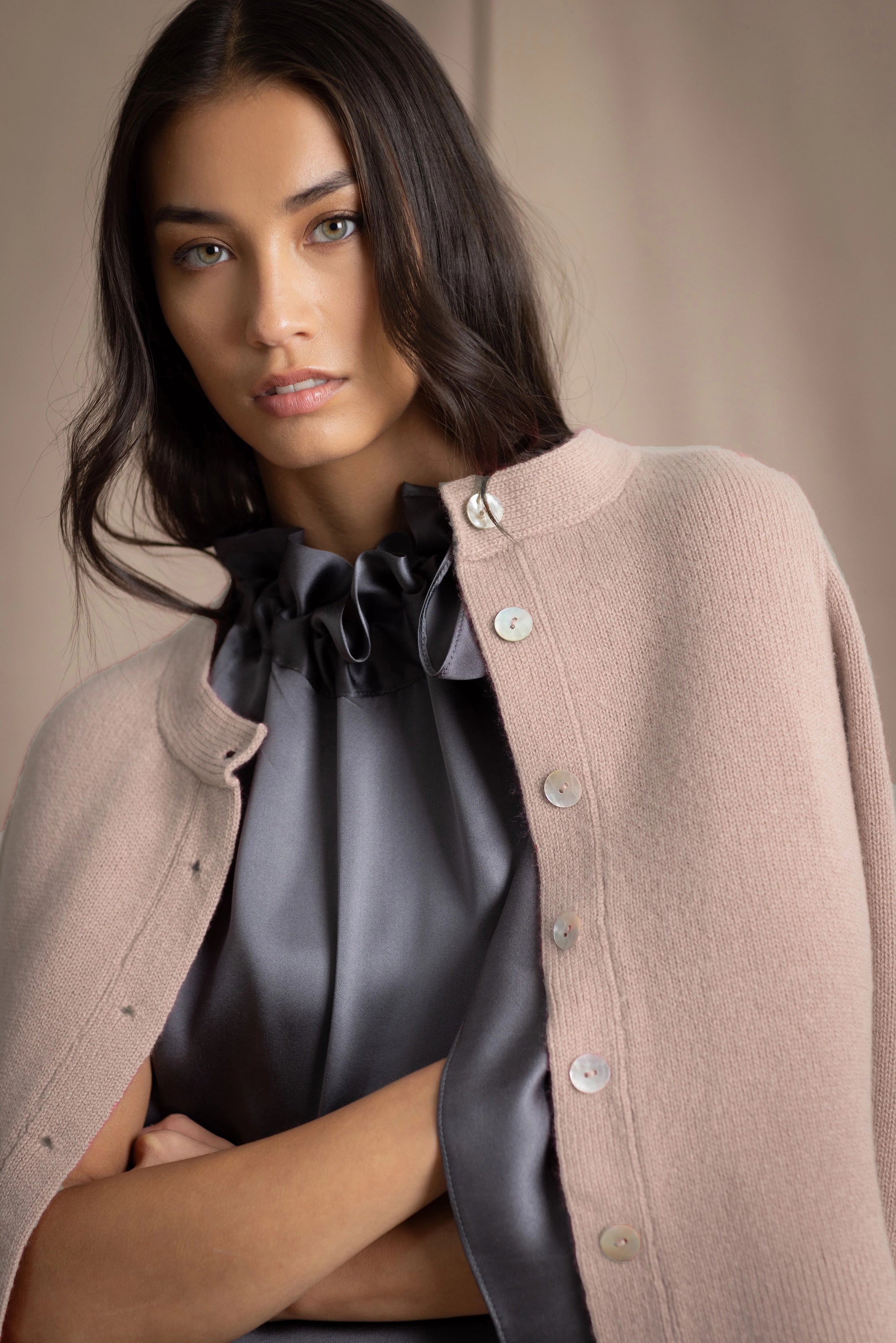 Woman wearing a beige cashmere cardigan with mother of pearl buttons over a grey pewter silk top