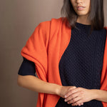 a woman wears an extra large cashmere wrap shawl in bright orange over navy cashmere aran sweater