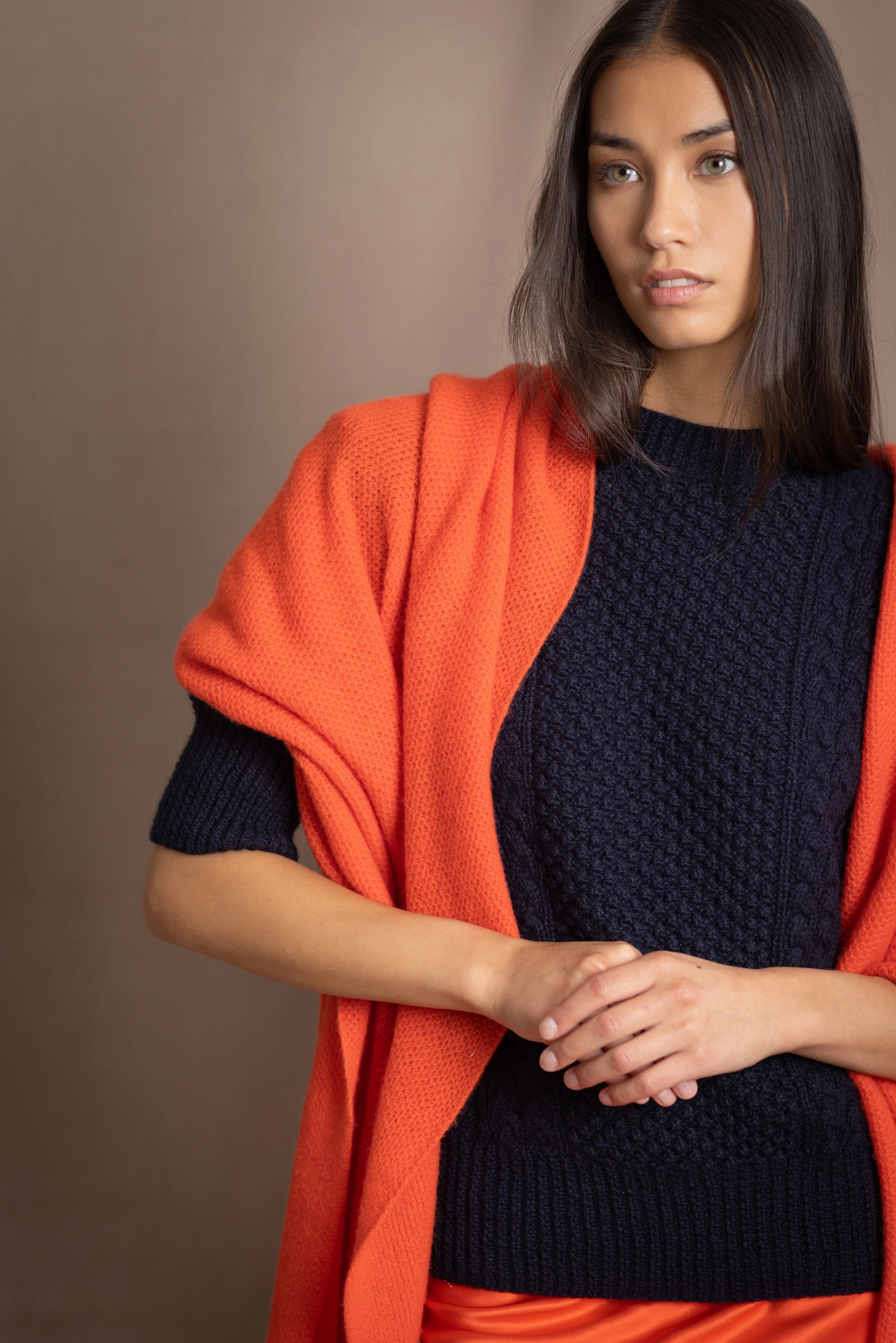 a woman wears an extra large cashmere wrap shawl in bright orange over navy cashmere aran sweater
