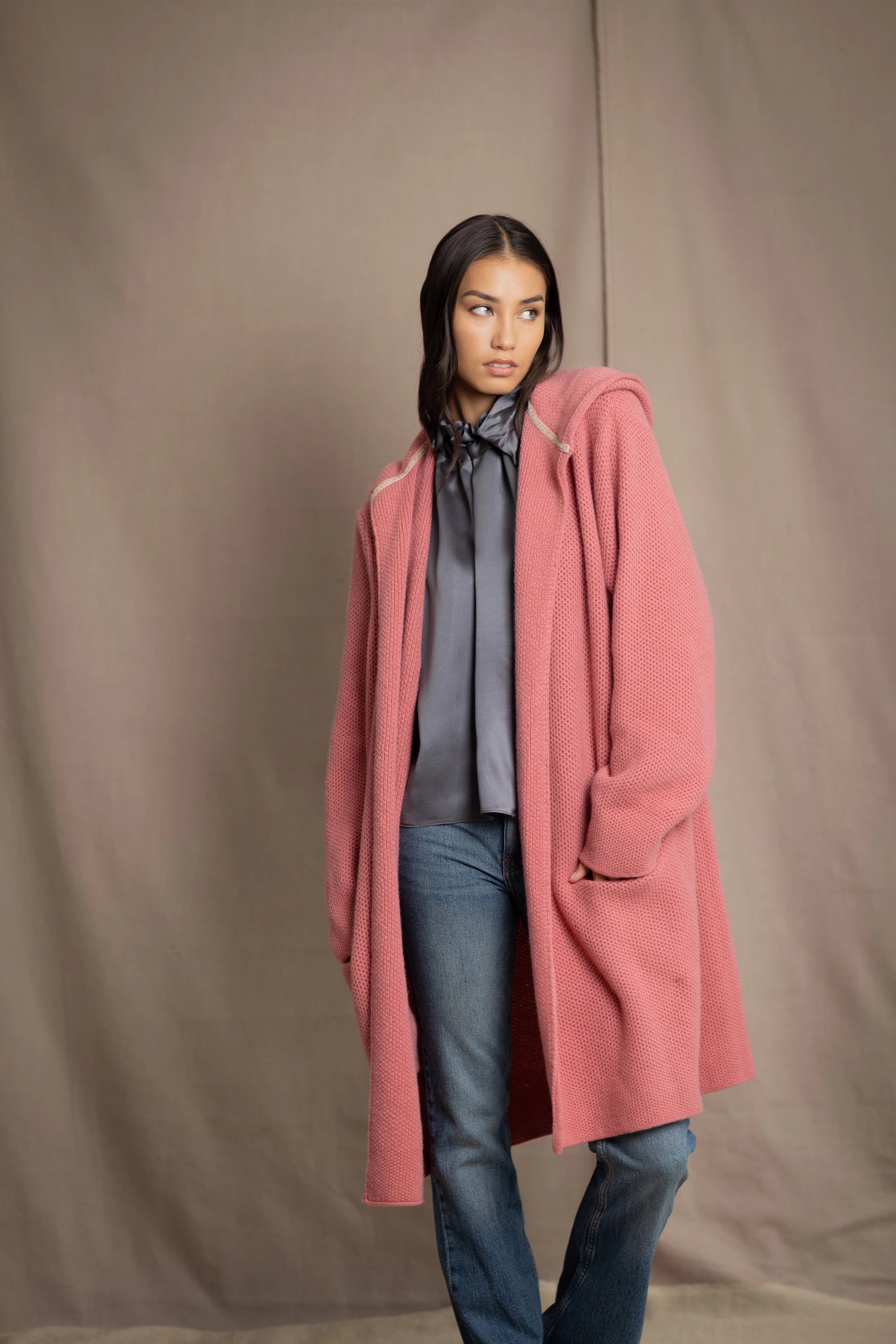 Woman wearing a long cashmere coat in dusty rose pink over a pewter gray silk top and blue jeans