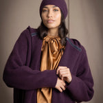 Woman wearing a long purple cashmere coat, bronze silk blouse with dark purple cashmere beanie hat