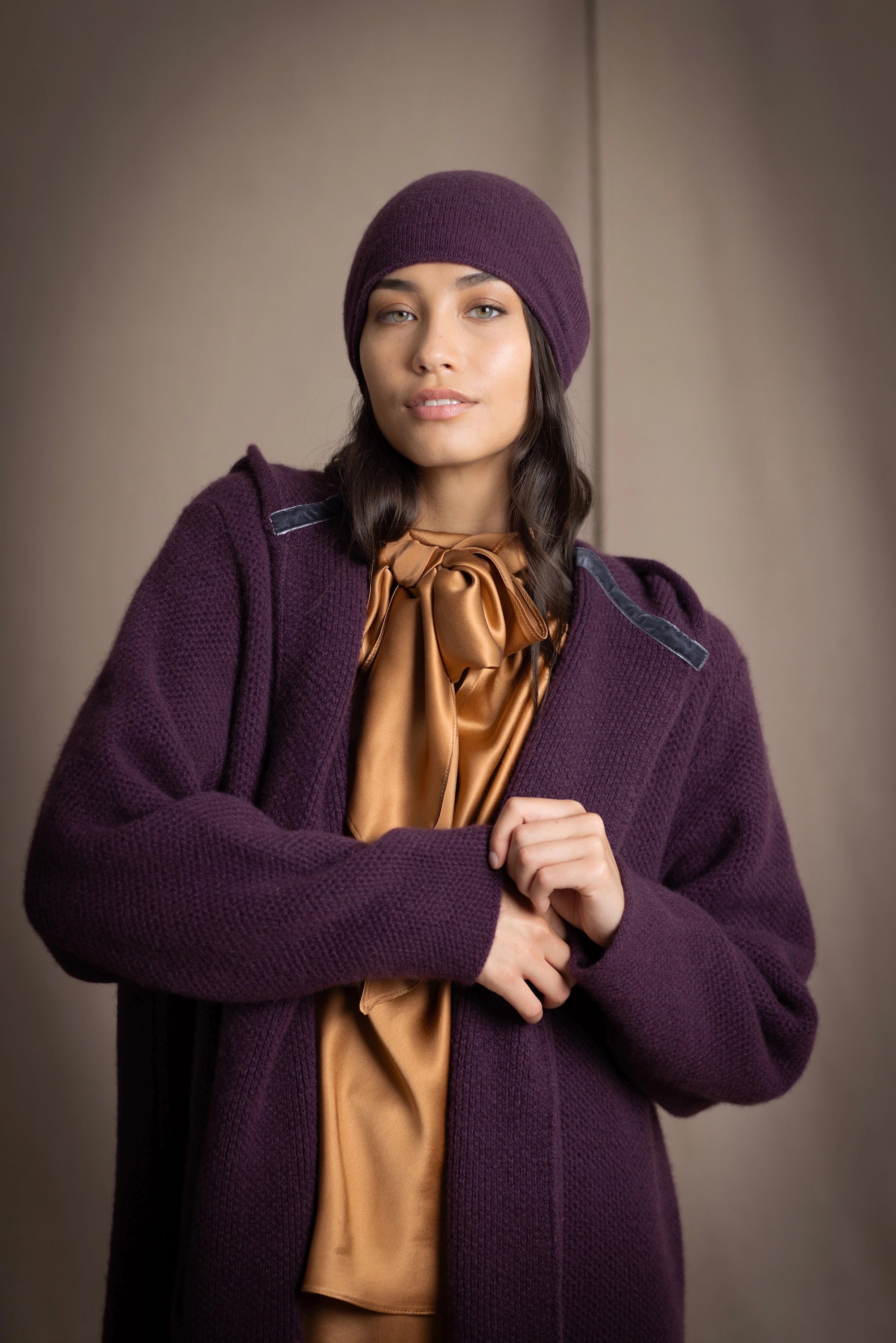 Woman wearing a long purple cashmere coat, bronze silk blouse with dark purple cashmere beanie hat
