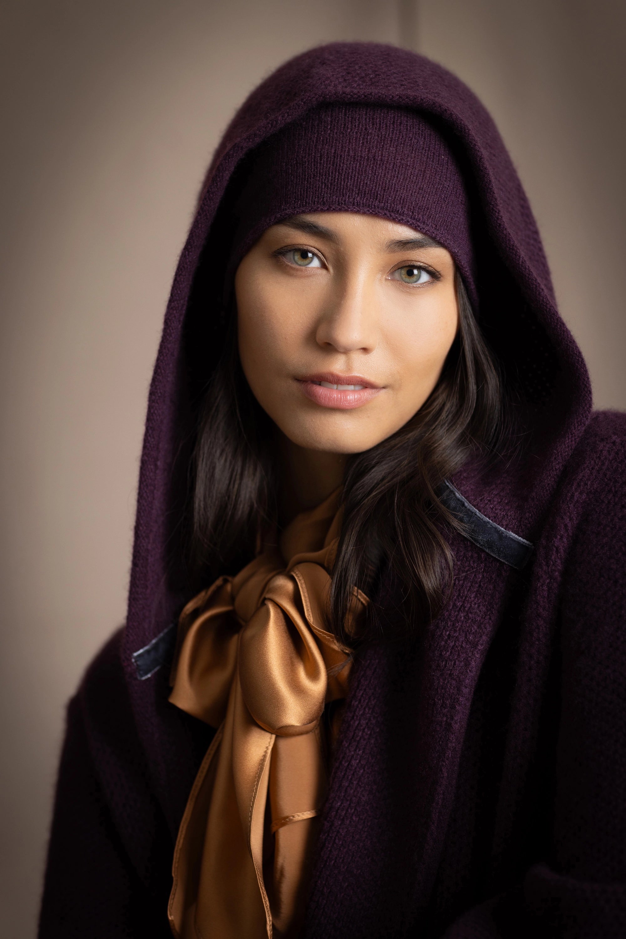 Woman wearing a long purple cashmere coat, bronze silk blouse with dark purple cashmere beanie hat