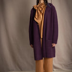 Woman wearing a long purple cashmere coat, bronze silk blouse and silk pants with dark purple cashmere beanie hat