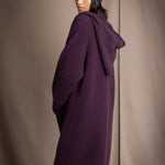 Woman wearing a long purple cashmere coat, bronze silk blouse and silk pants with dark purple cashmere beanie hat
