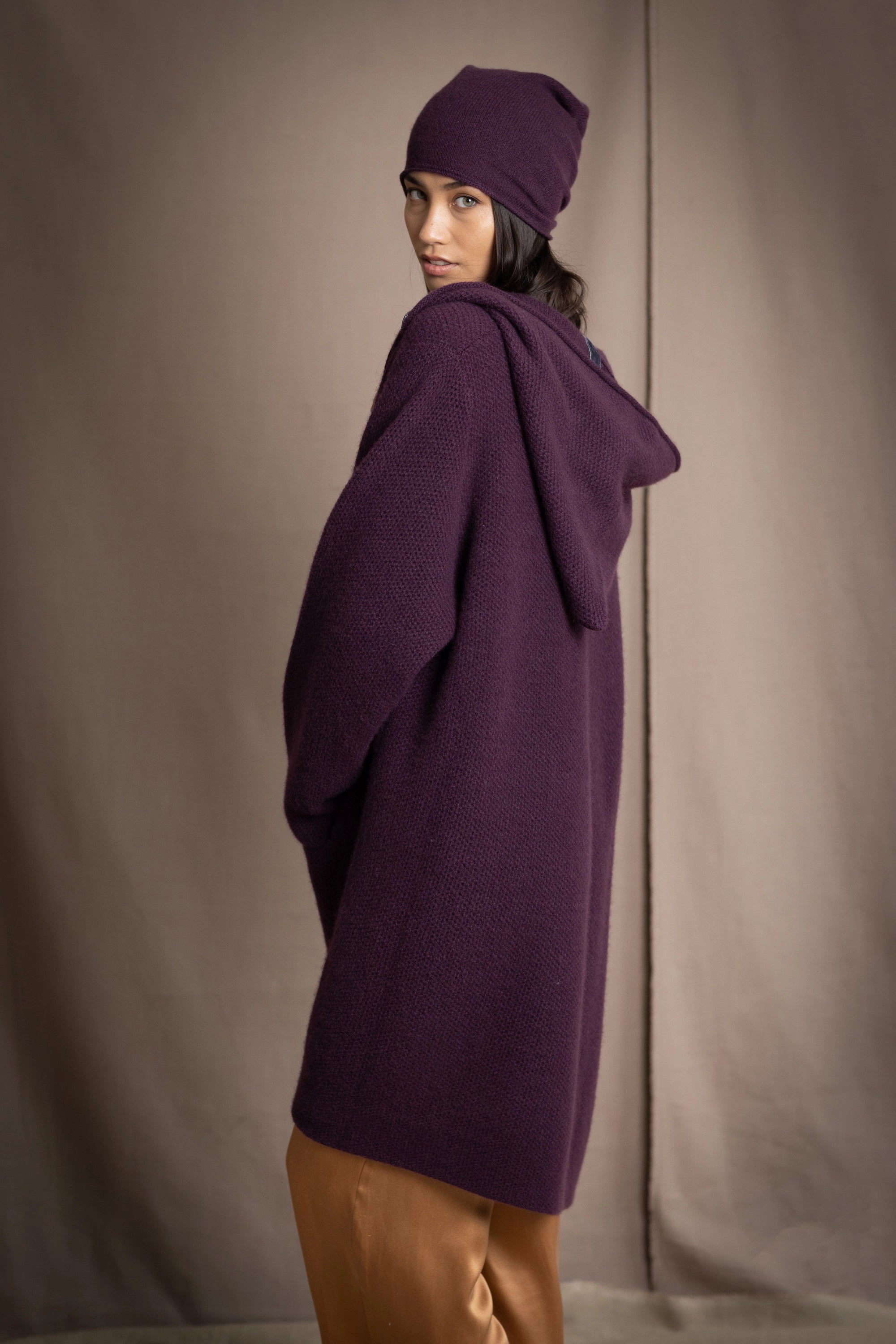 Woman wearing a long purple cashmere coat, bronze silk blouse and silk pants with dark purple cashmere beanie hat