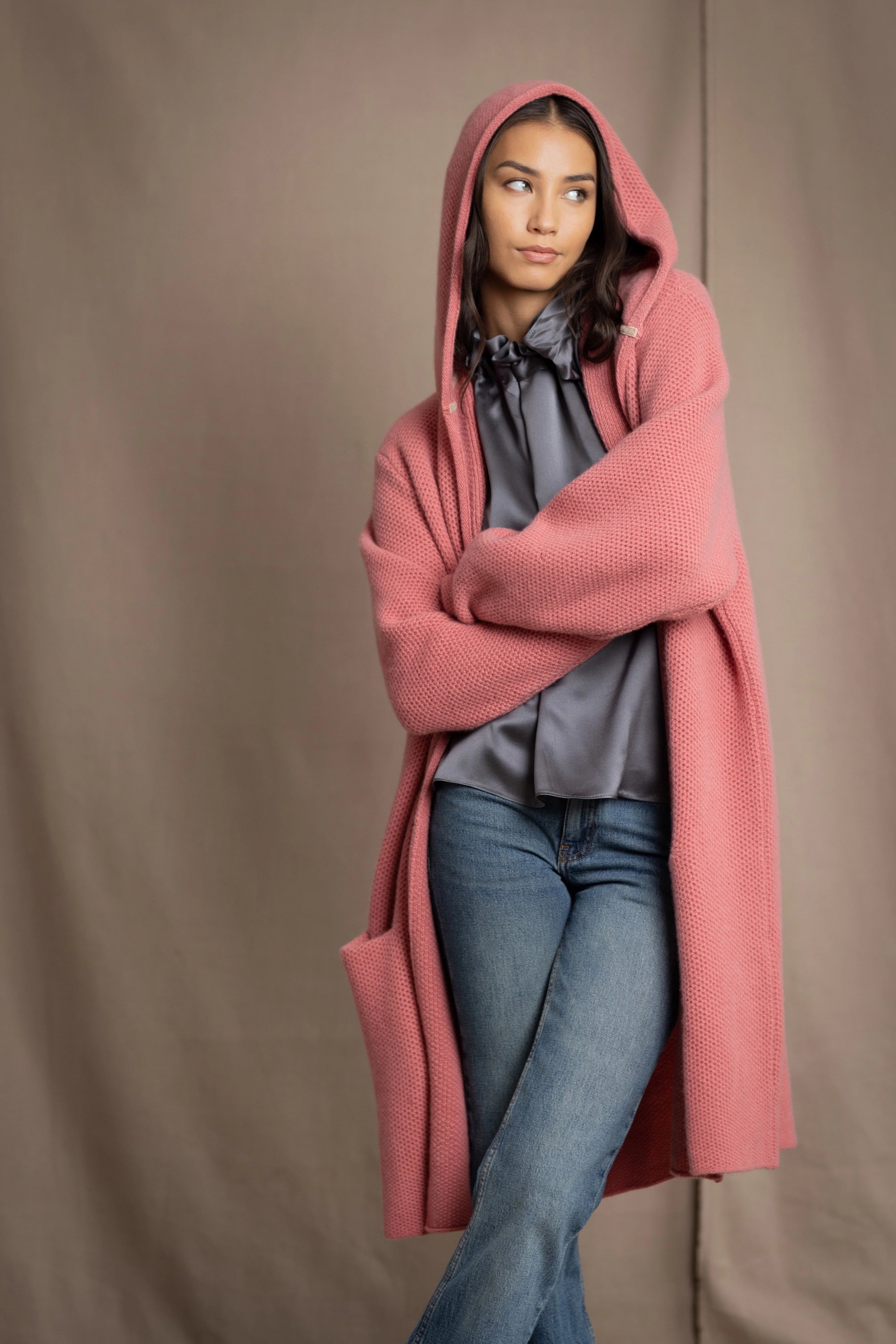 Woman wearing a long cashmere coat in dusty rose pink over a  pewter gray silk top and blue jeans