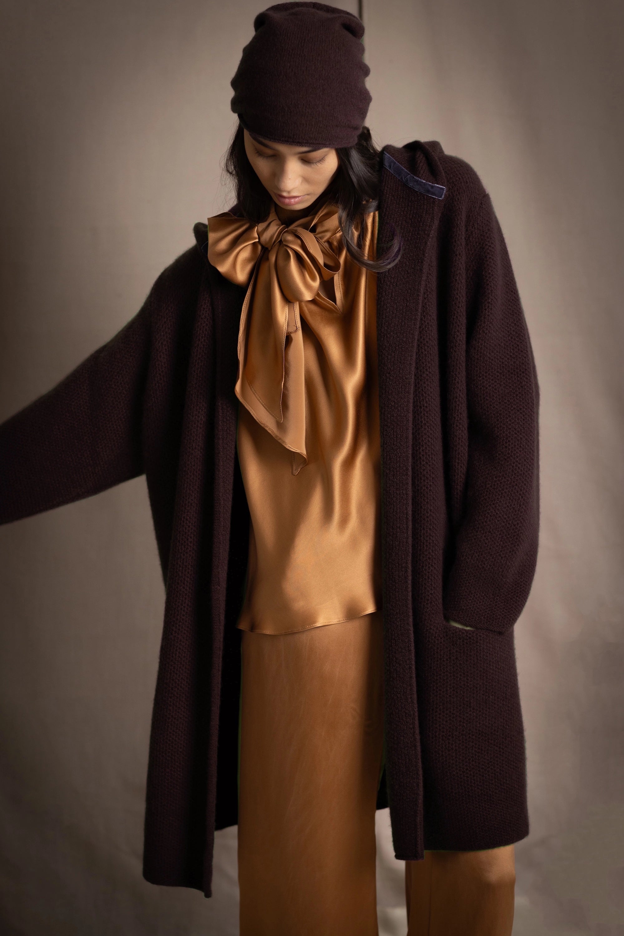 Person wearing a brown cashmere coat and cashmere hat with bronze silk clothing