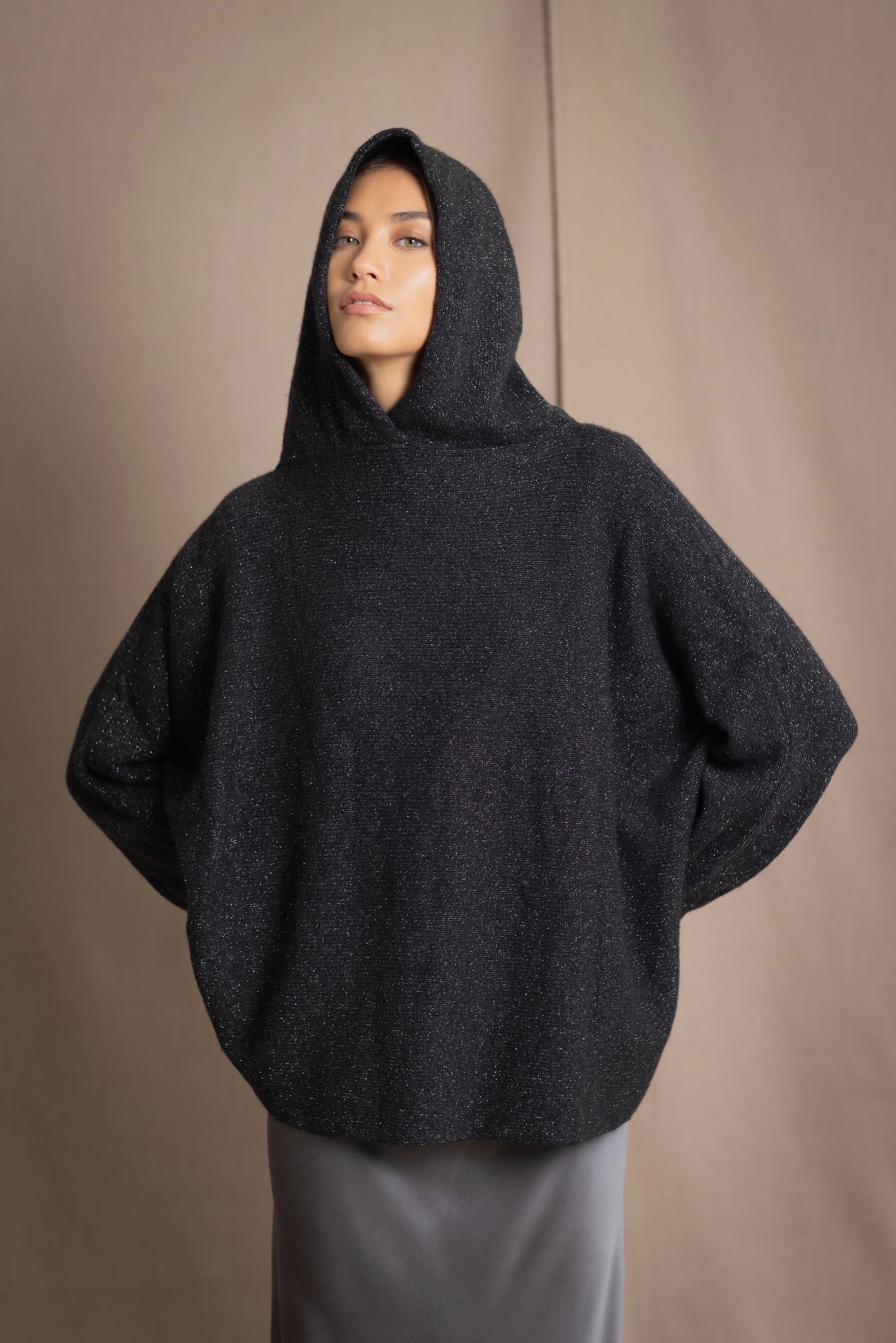 woman wearing an oversized cashmere sweater with hood in black and silver sparkly metallic colour and dark grey skirt