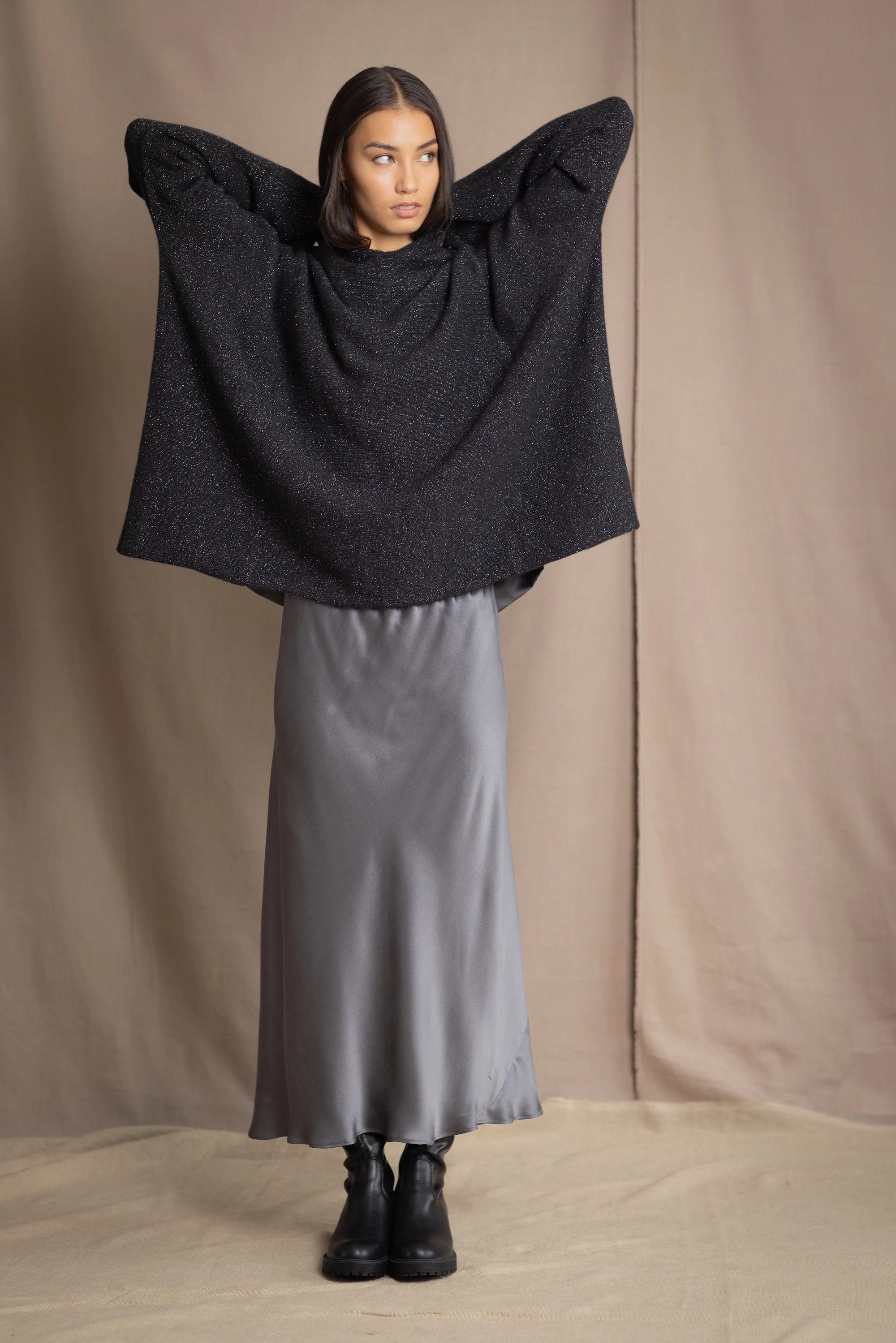 woman wearing an oversized cashmere sweater with hood in black and silver sparkly metallic colour with dark grey silk skirt and black leather boots