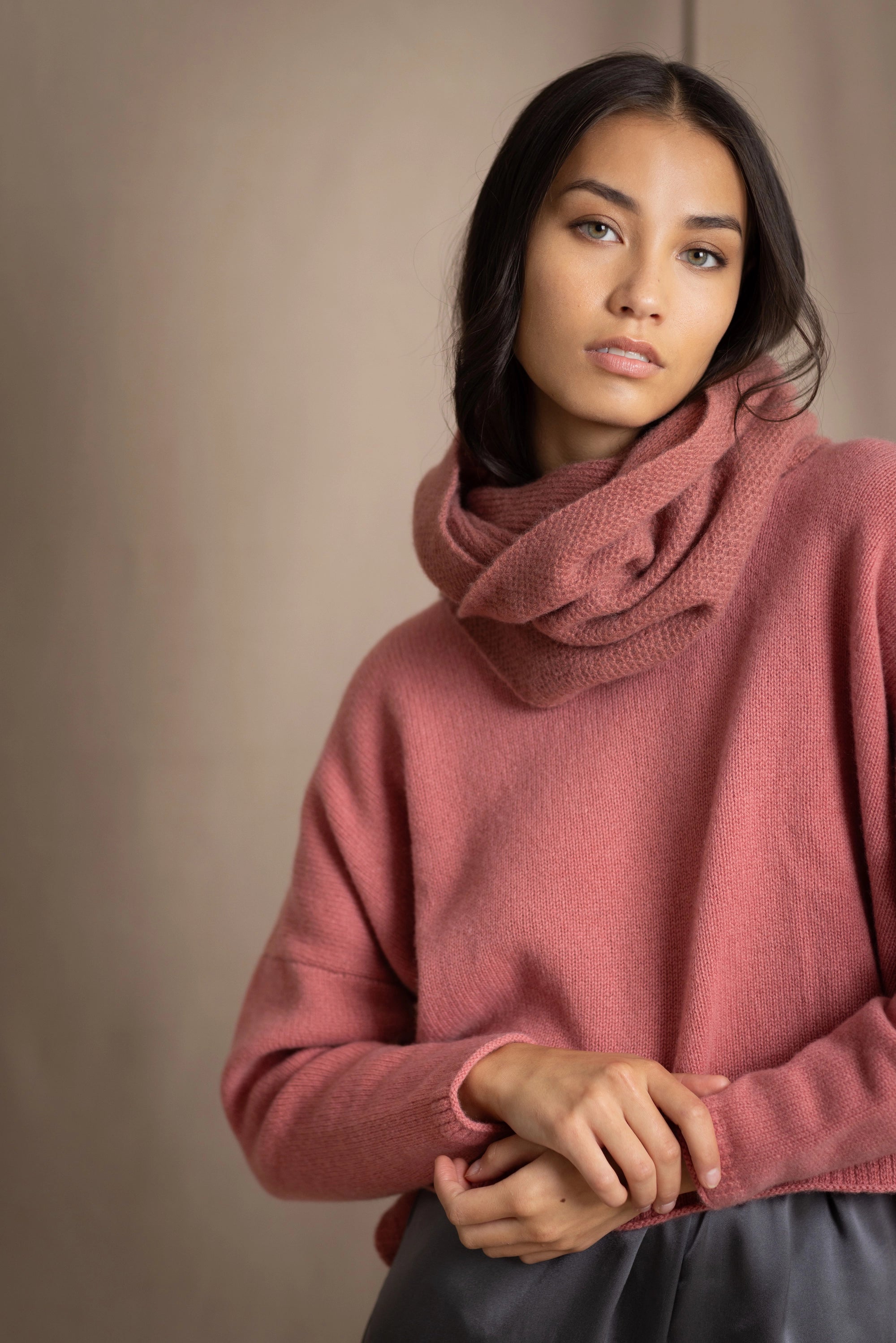 a woman wearing a cropped cashmere oversized cashmere sweater in dusty rose pink with matching cashmere snood over silk trousers in pewter grey