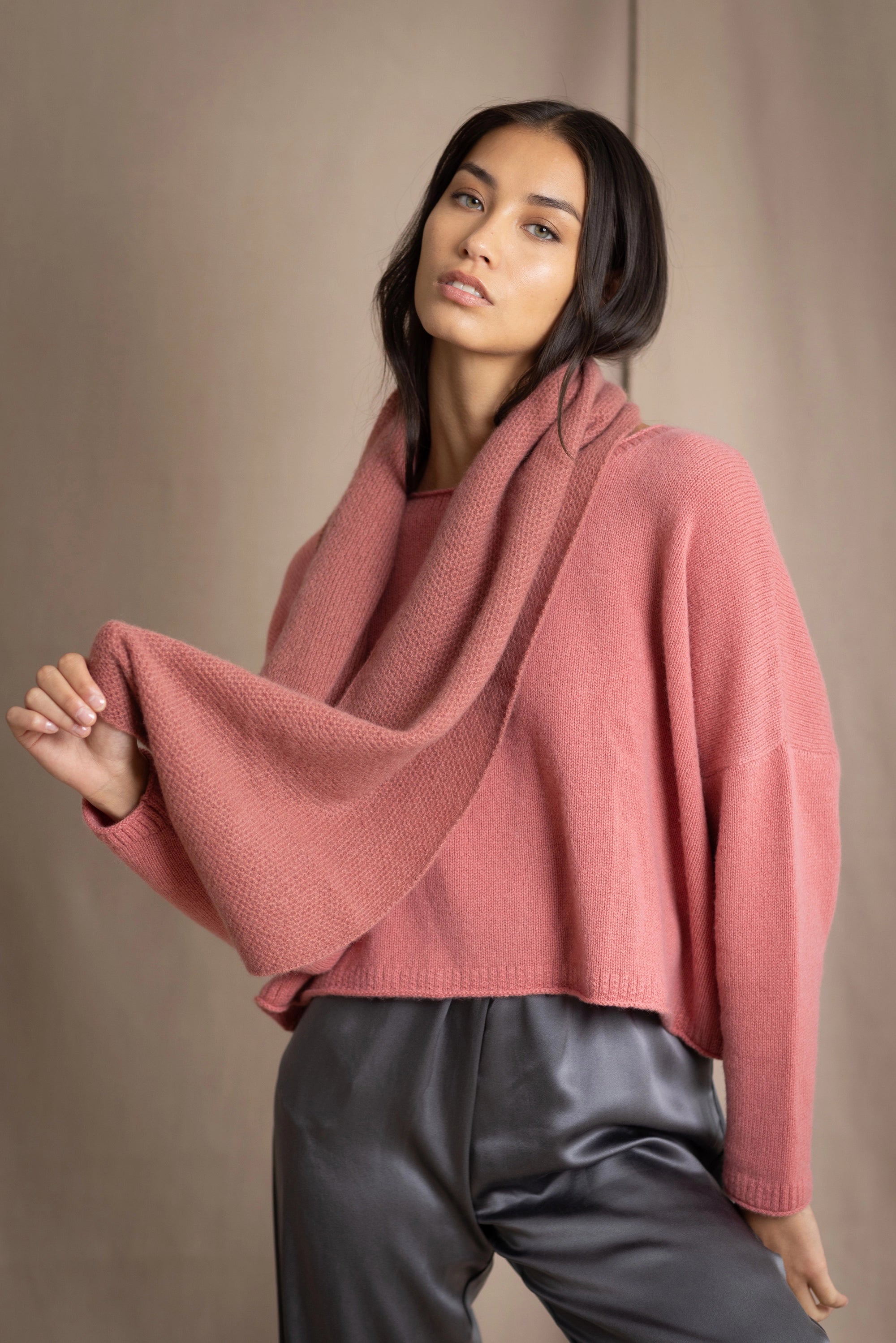 a woman wearing a cropped cashmere oversized cashmere sweater in dusty rose pink with matching cashmere snood over silk trousers in pewter grey