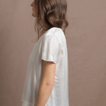 A woman wears a 100% silk v-neck t-shirt in white with a pair of jeans