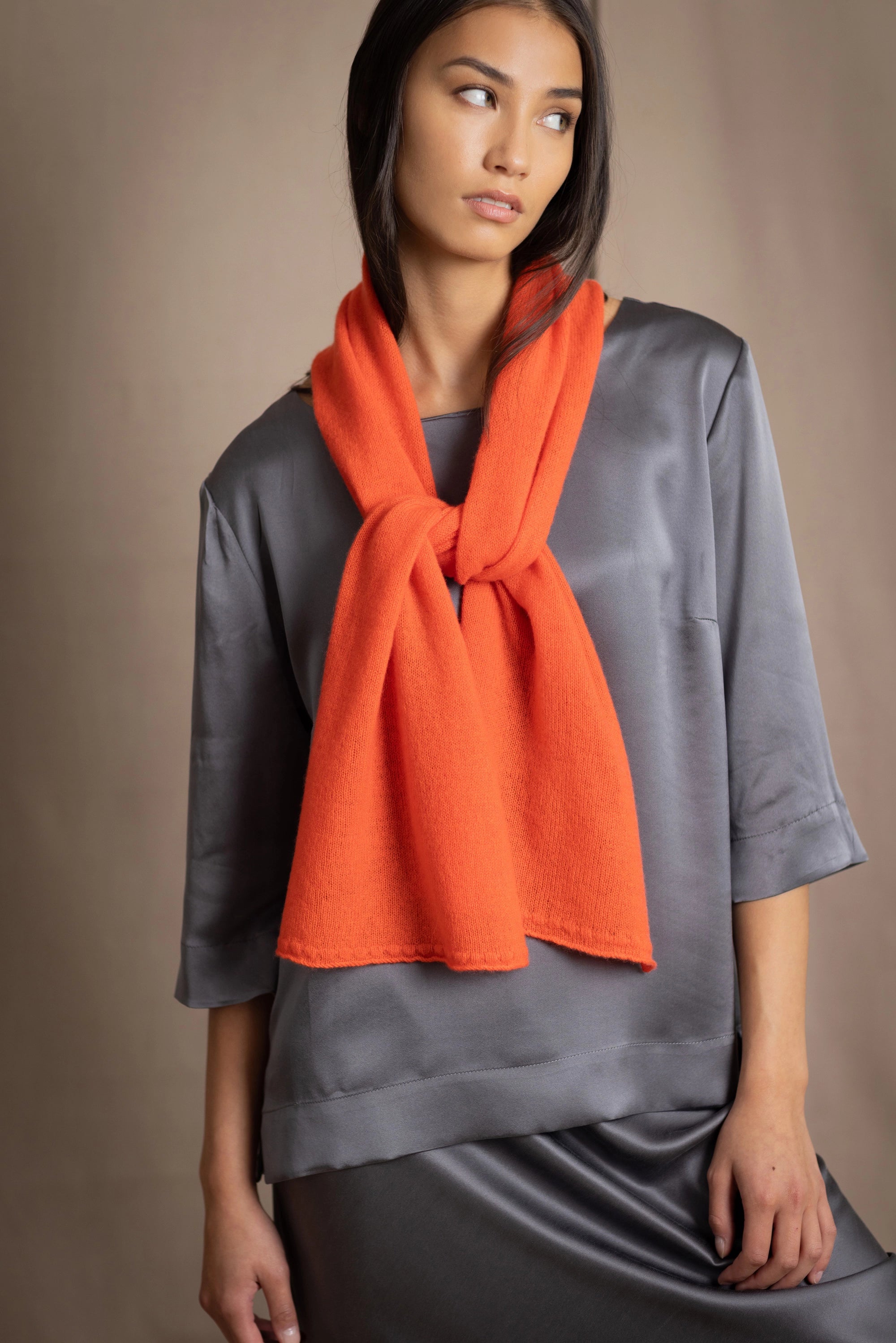 woman wearing a bright orange cashmere scarf over pewter grey silk clothing