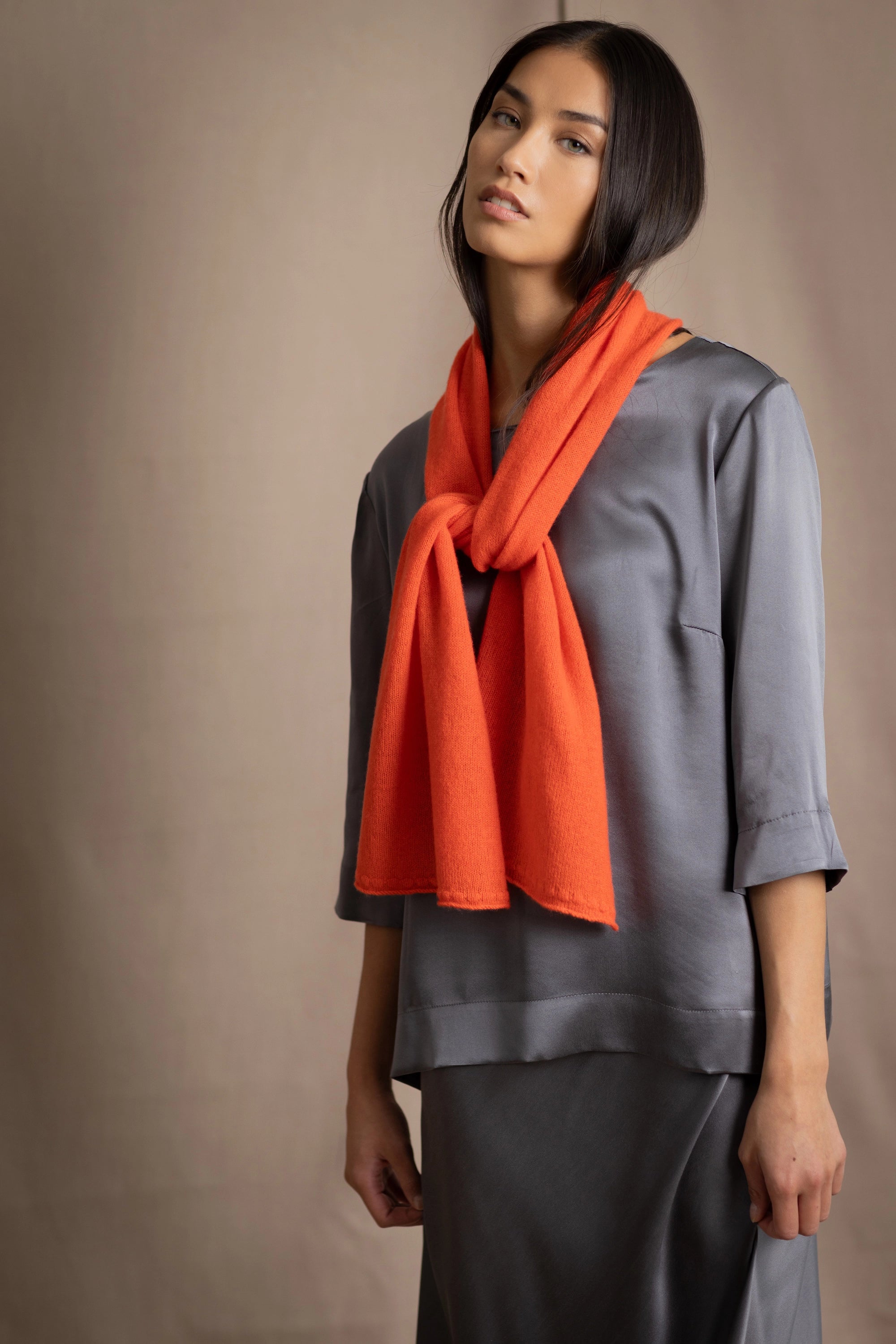 woman wearing a bright orange cashmere scarf over pewter grey silk clothing