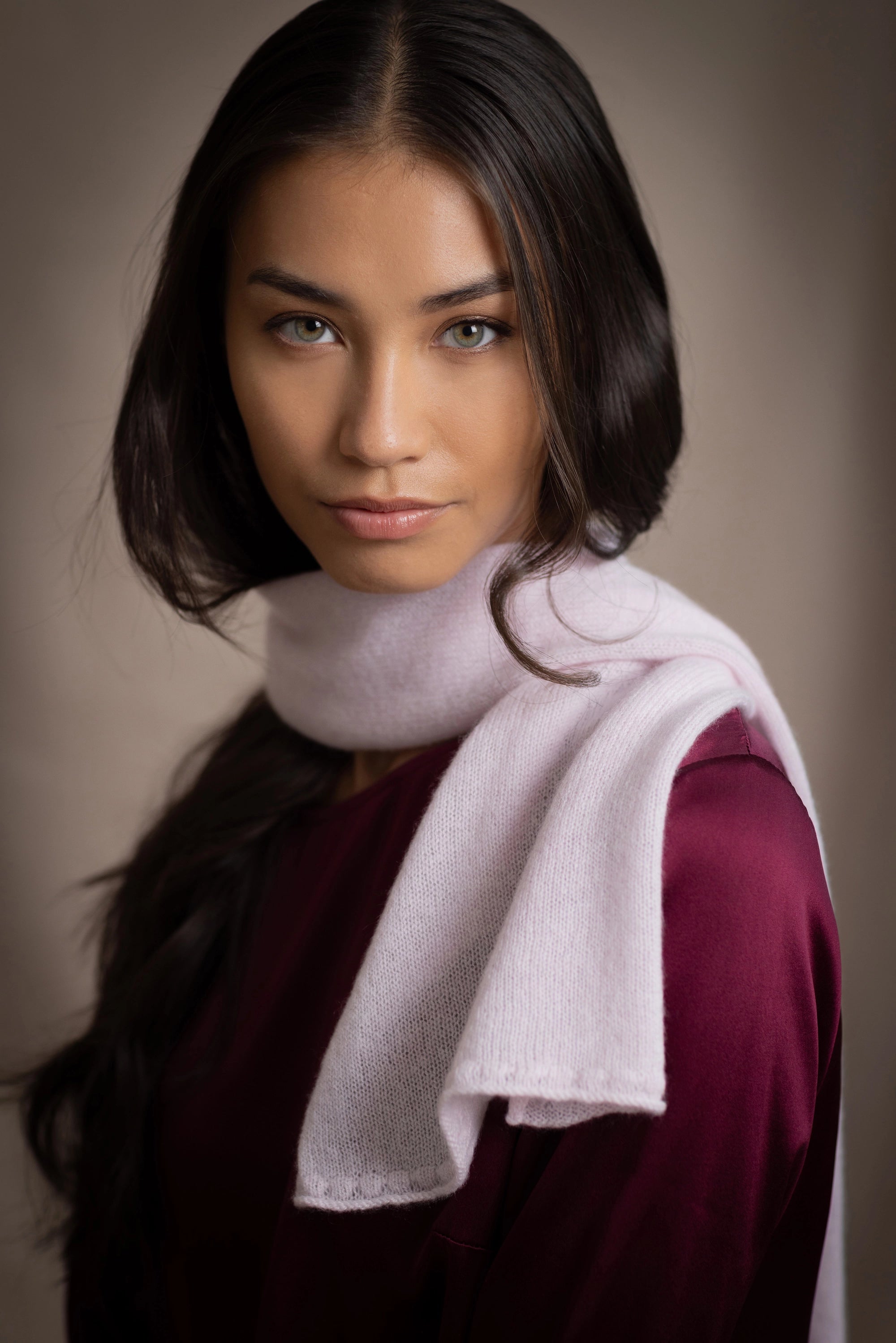 a woman wears a small cashmere scarf in pale pink worn over burgundy silk clothing