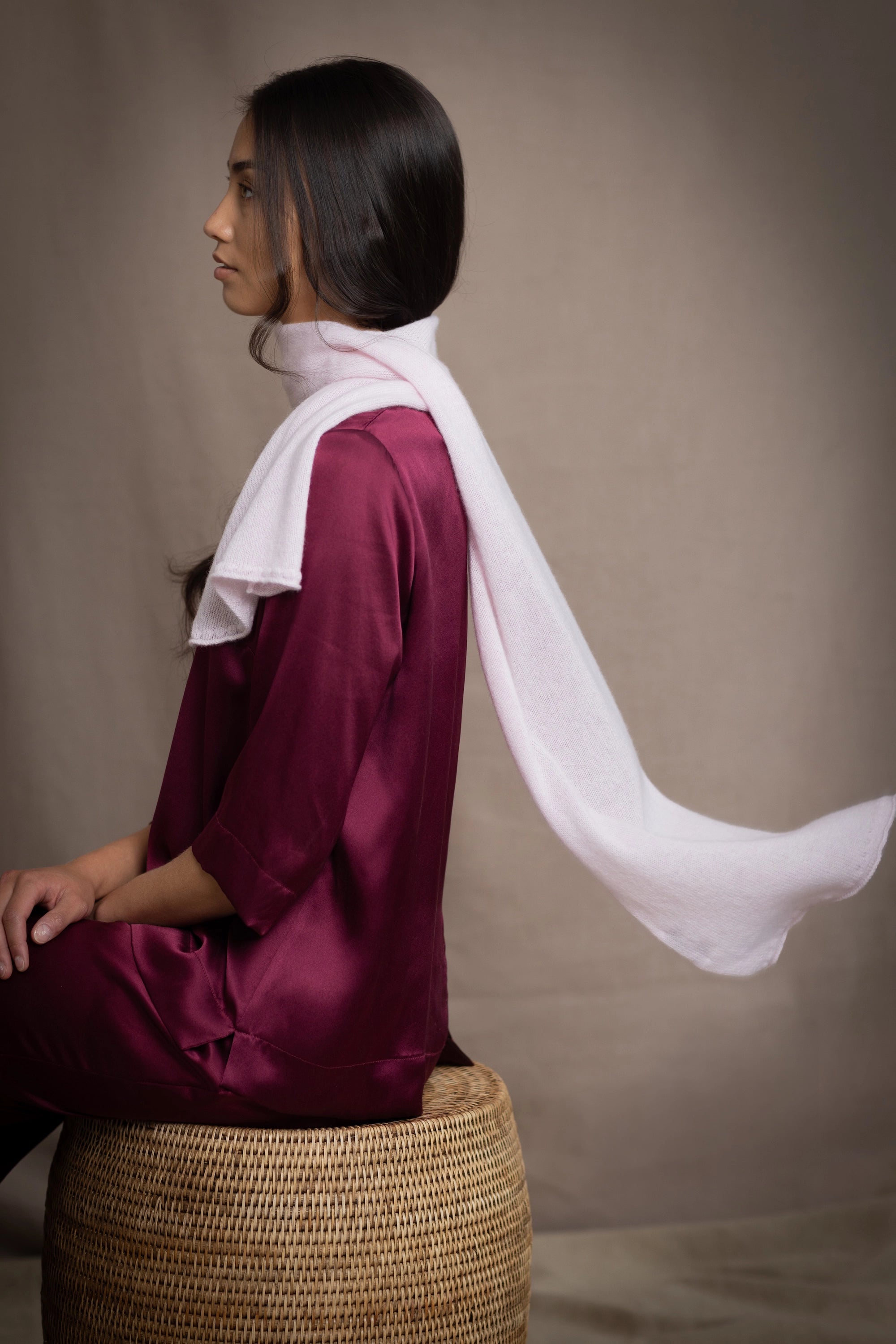 a woman wears a small cashmere scarf in pale pink worn over burgundy silk clothing