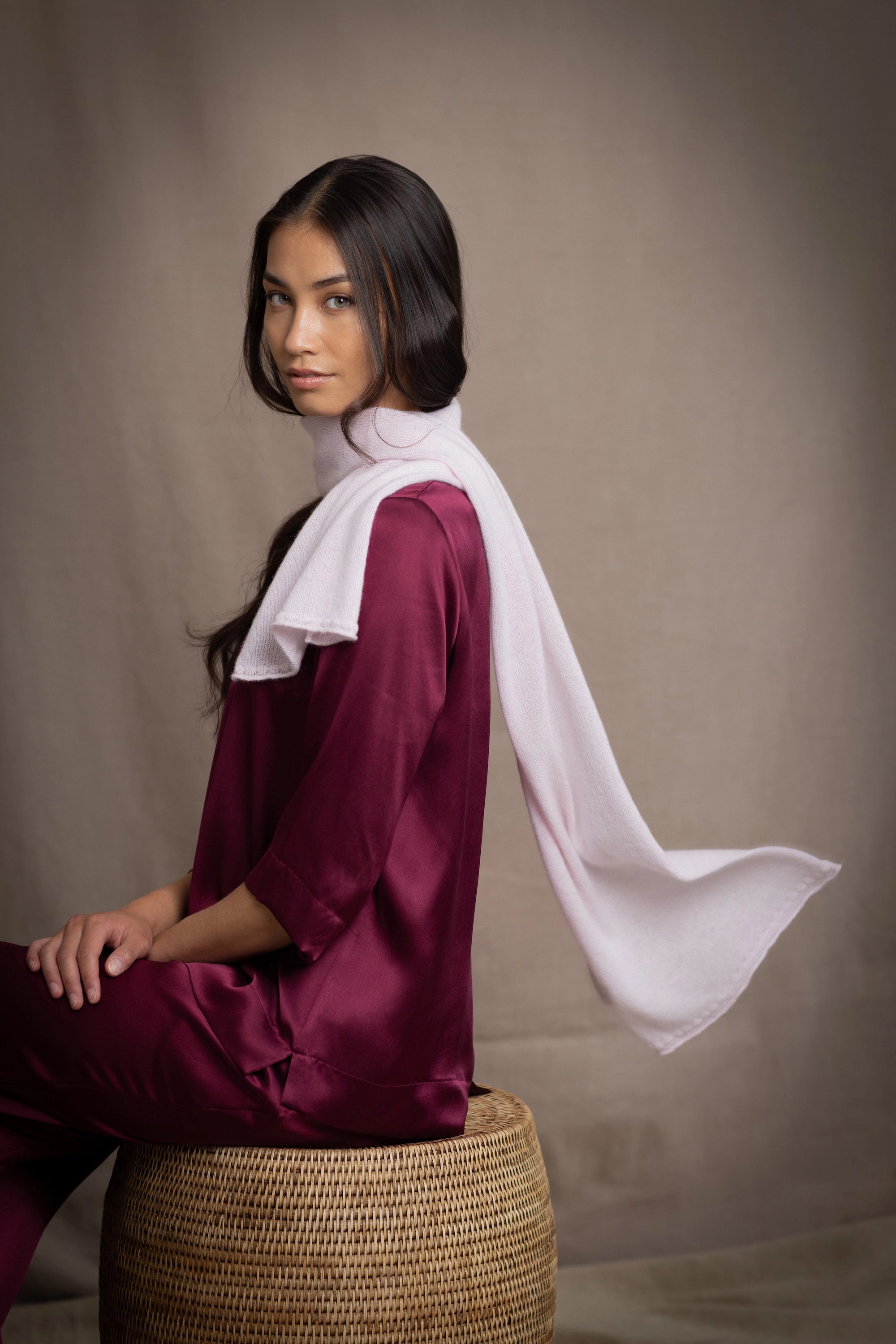a woman wears a small cashmere scarf in pale pink worn over burgundy silk clothing