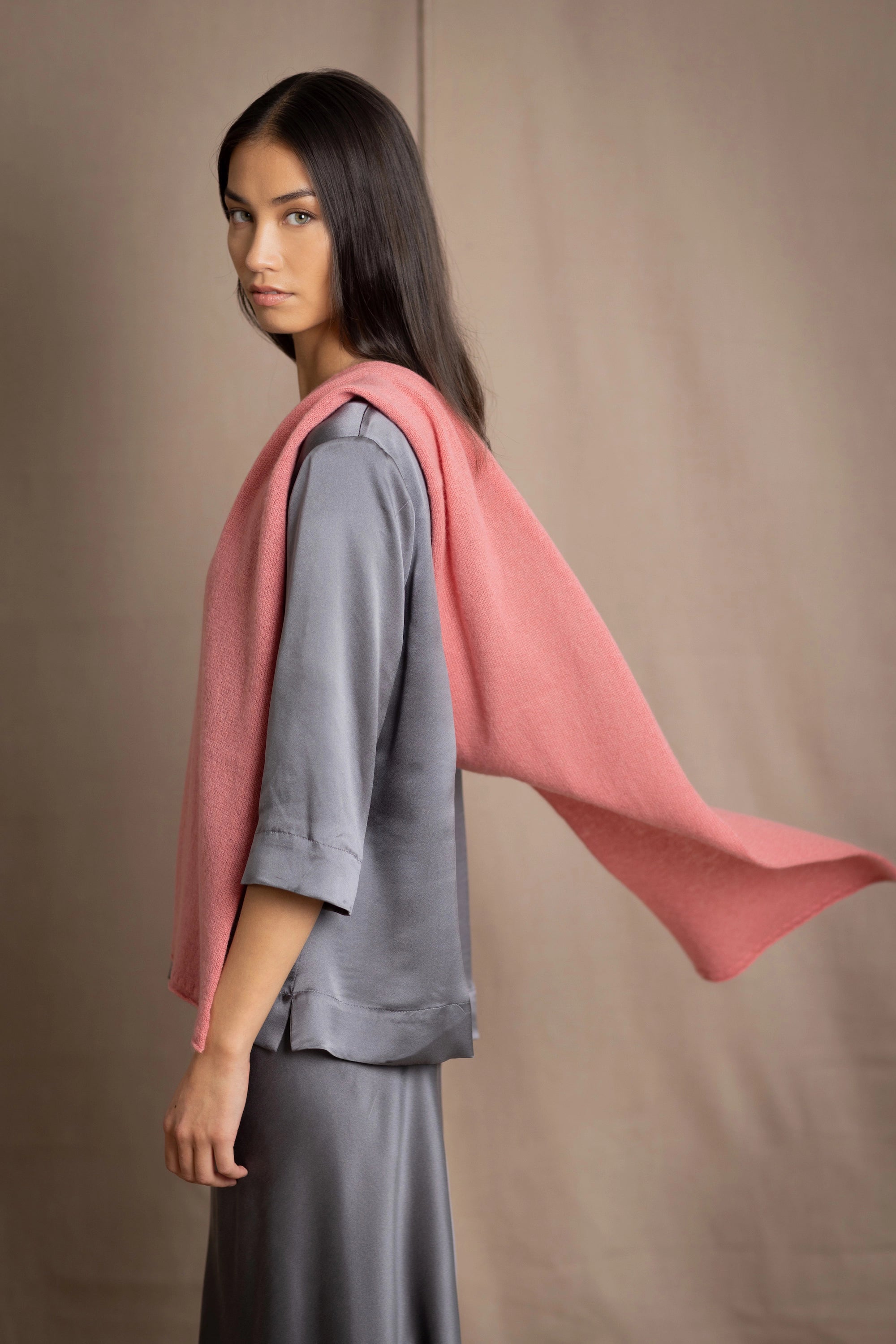a woman wearing a cashmere scarf in dusty rose pink with a cashmere beanie hat over grey pewter silk clothing