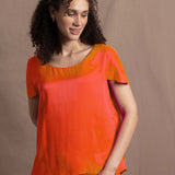 a woman wears a bright orange crew neck short sleeve silk tee and matching trousers