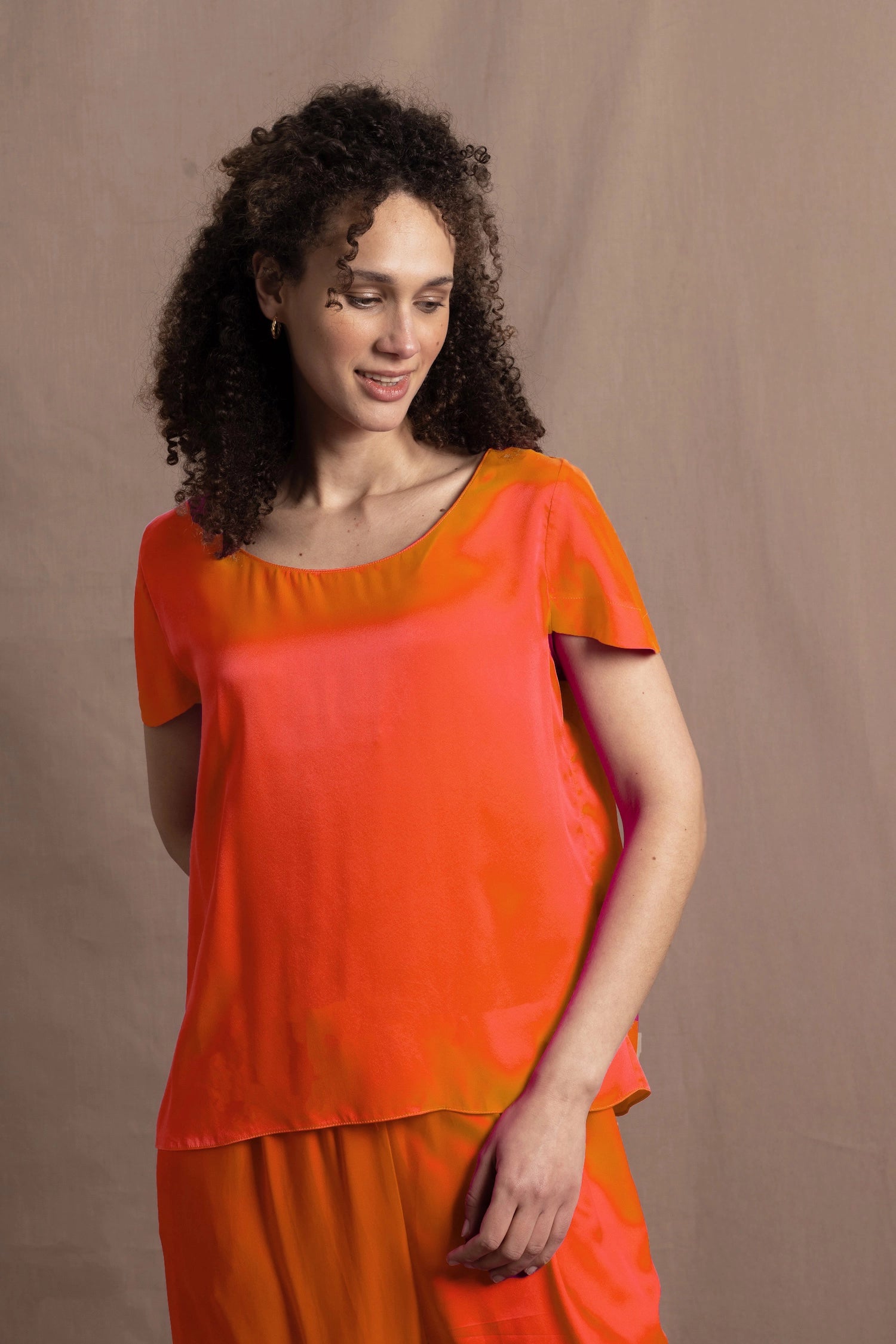 a woman wears a bright orange crew neck short sleeve silk tee and matching trousers
