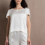 A lady wears a crew neck silk t-shirt in white with butterfly sleeves and matching silk shorts