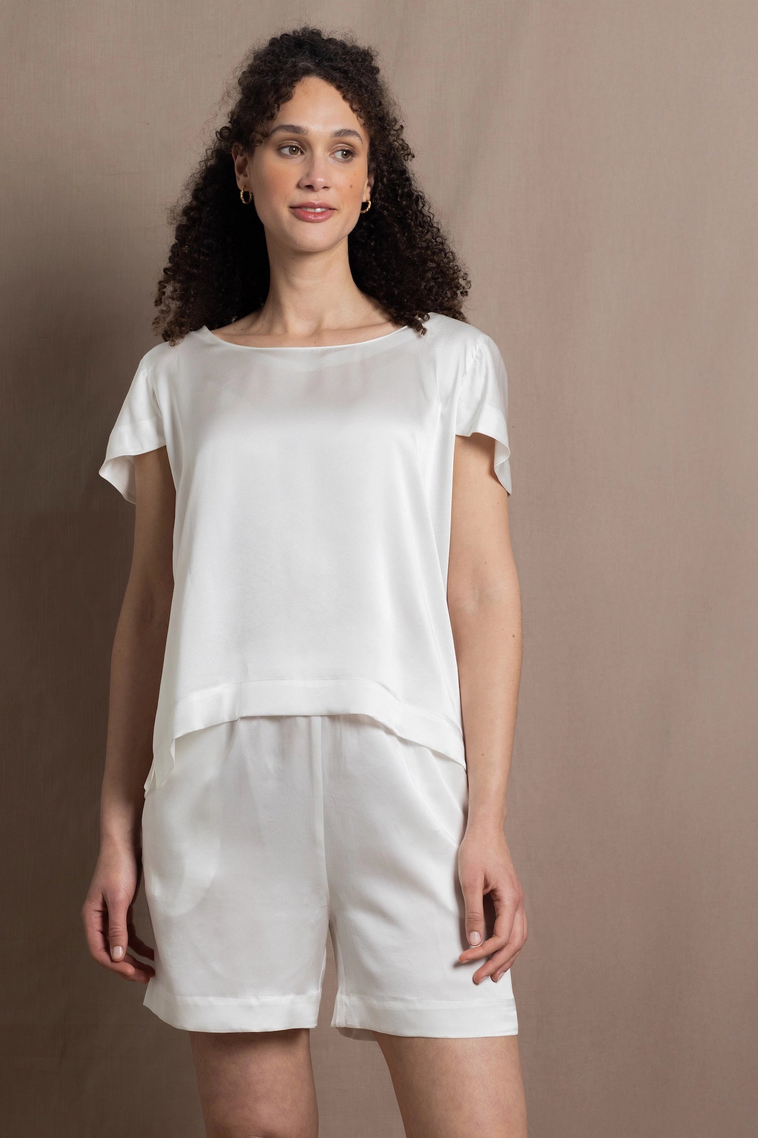 A lady wears a crew neck silk t-shirt in white with butterfly sleeves and matching silk shorts