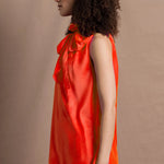 a woman wears a bright orange silk sleeveless top with bow around the neck and matching silk trousers