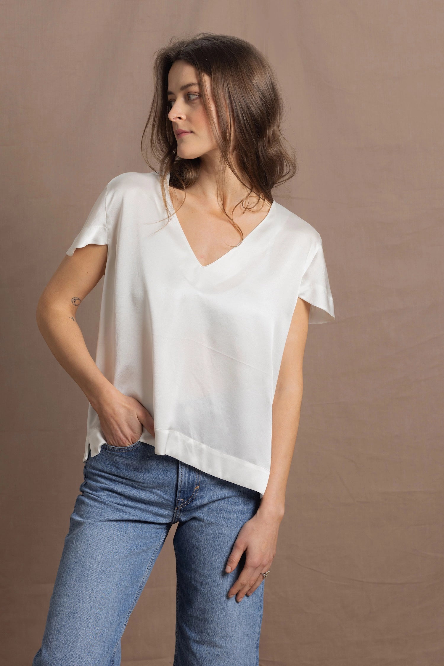 A woman wears a 100% silk v-neck t-shirt in white with a pair of jeans