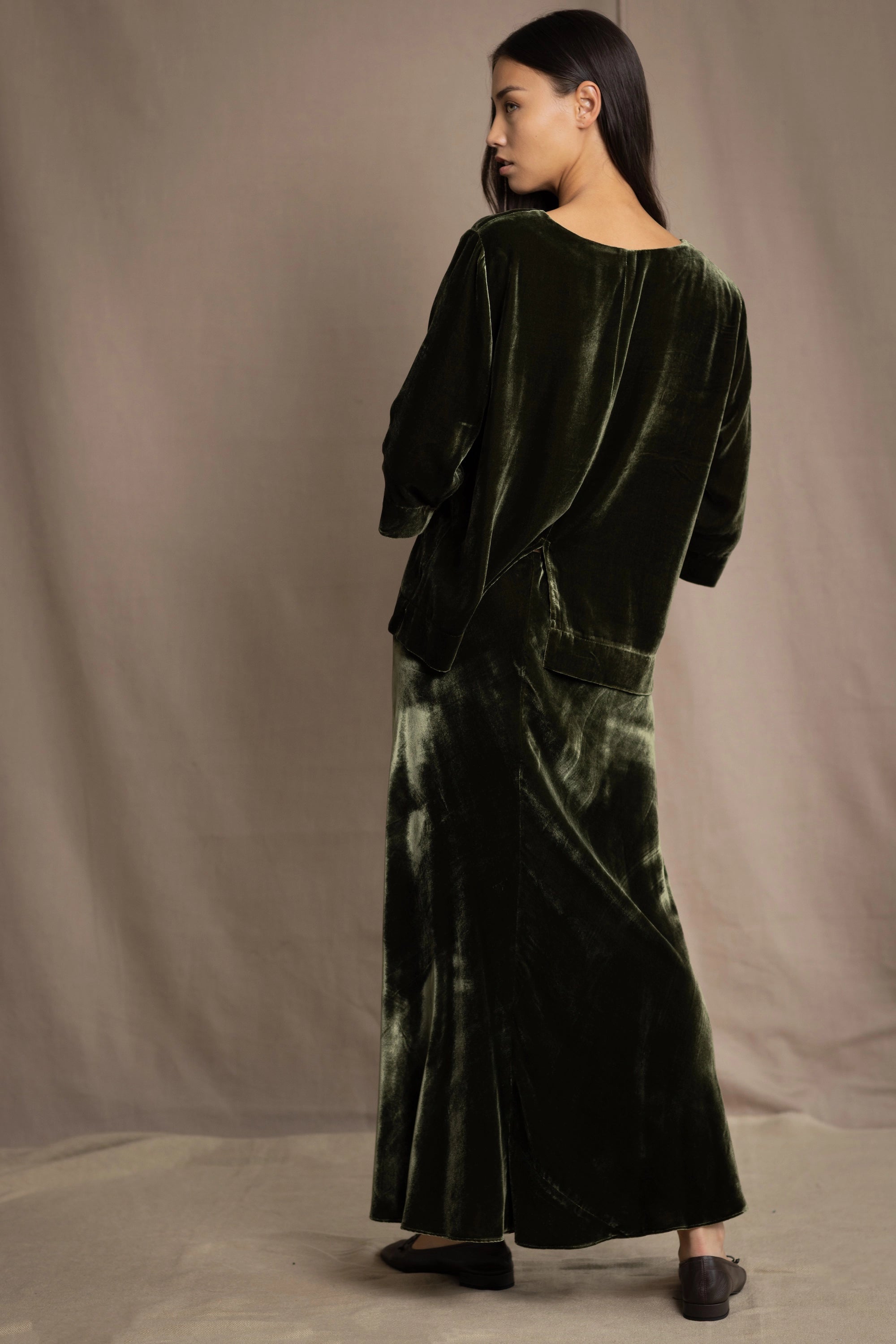 a woman wears a 3/4 sleeve top in silk velvet in olive green with silk velvet skirt