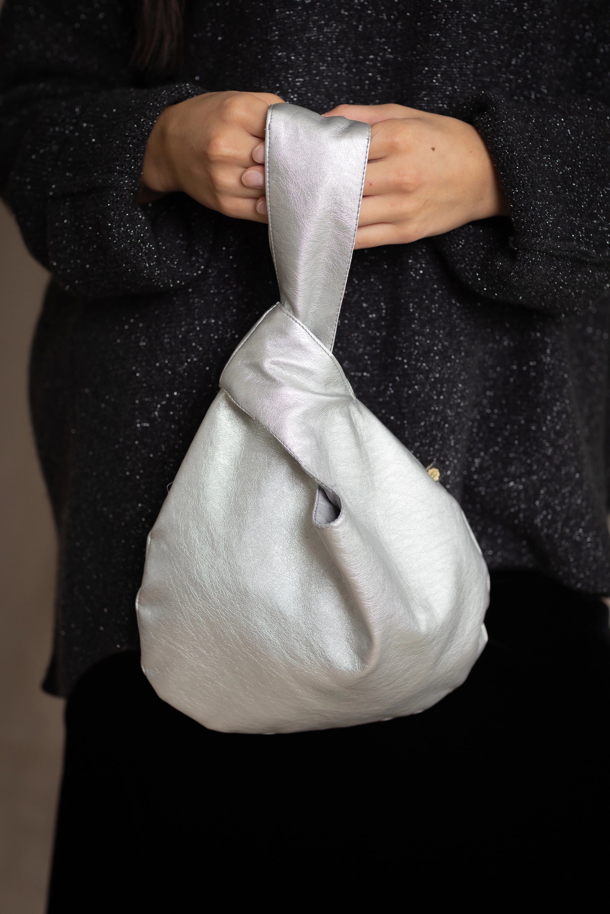 Silver vegan leather pull through handbag held by a person wearing a dark sparkly sweater