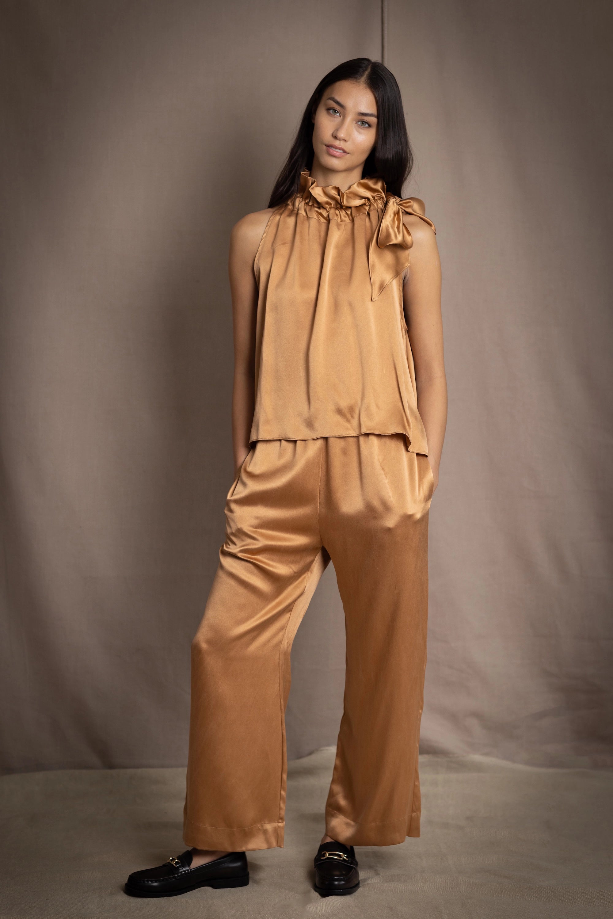 a woman wearing bronze silk trousers and matching halter top  with loafers
