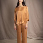 woman wearing a bronze silk 3/4 sleeve top blouse with matching silk trousers and dark brown loafers