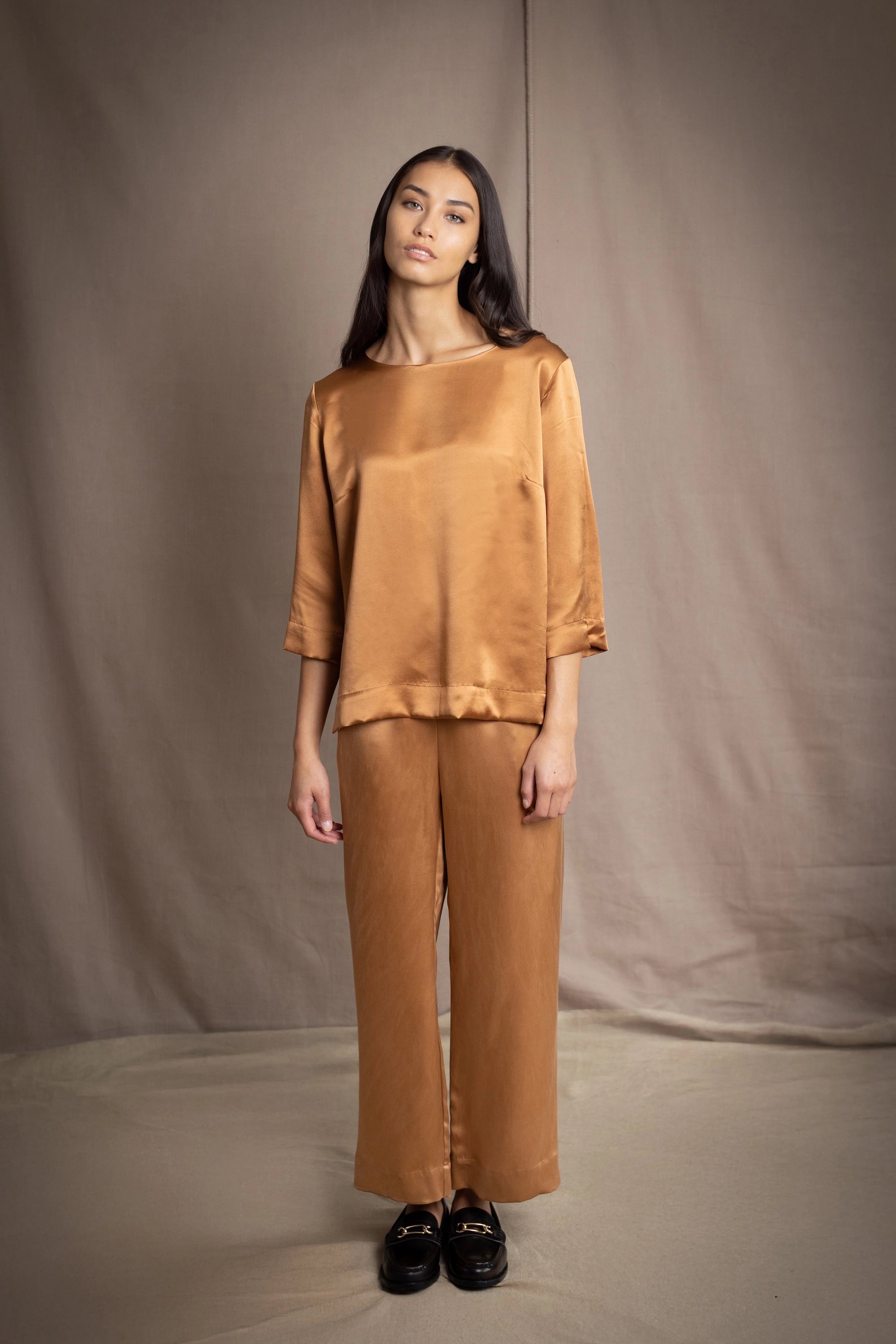 woman wearing a bronze silk 3/4 sleeve top blouse with matching silk trousers and dark brown loafers