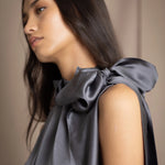 Woman wearing a dark gray sleeveless silk blouse with a bow and halter neck
