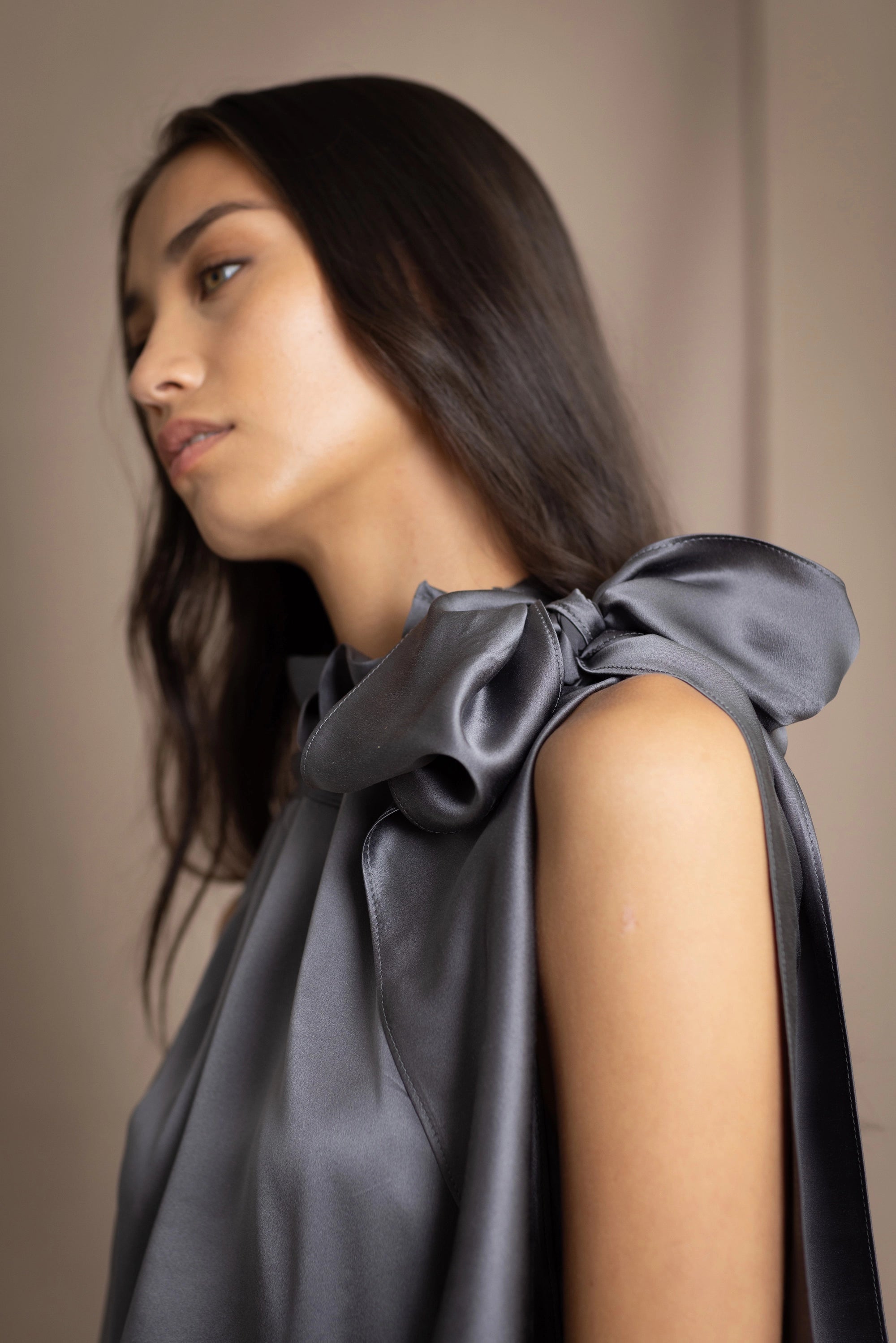 Woman wearing a dark gray sleeveless silk blouse with a bow and halter neck