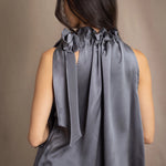 Woman wearing a dark gray sleeveless silk blouse with a bow and halter neck detail